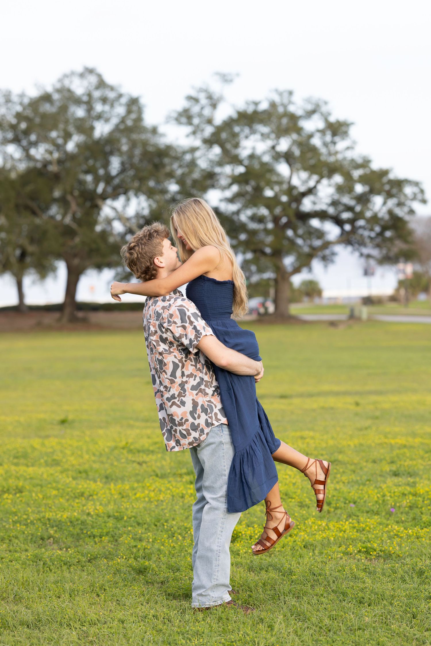A couple embraces in a romantic hug while standing in a green field filled with yellow wildflowers.