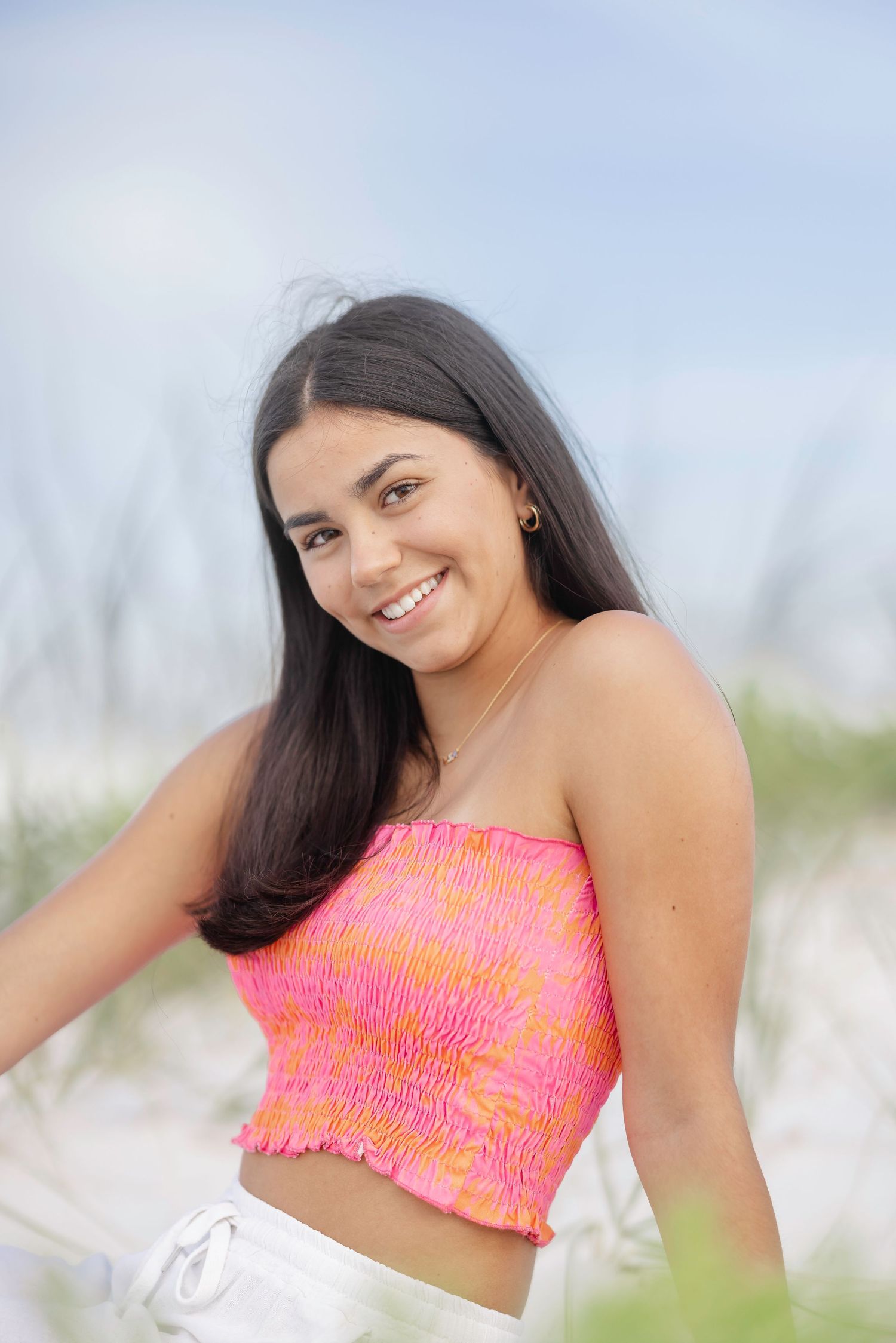 A person wearing a bright coral pink smocked top poses outdoors in a series of four casual portraits.