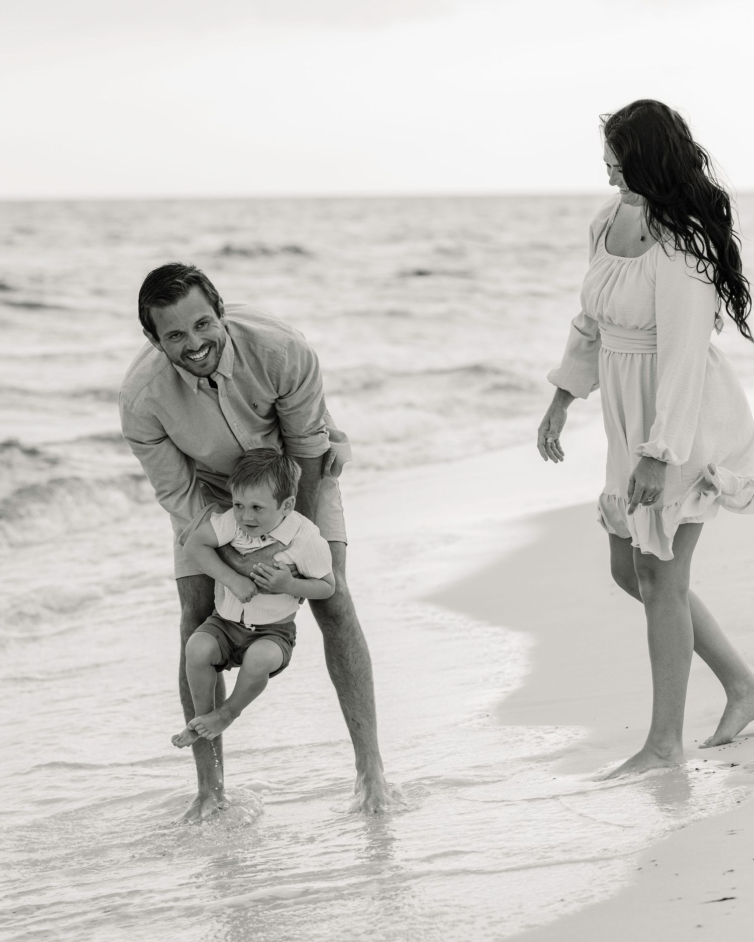 Family playing in ocean waves together at the beach in black and white.