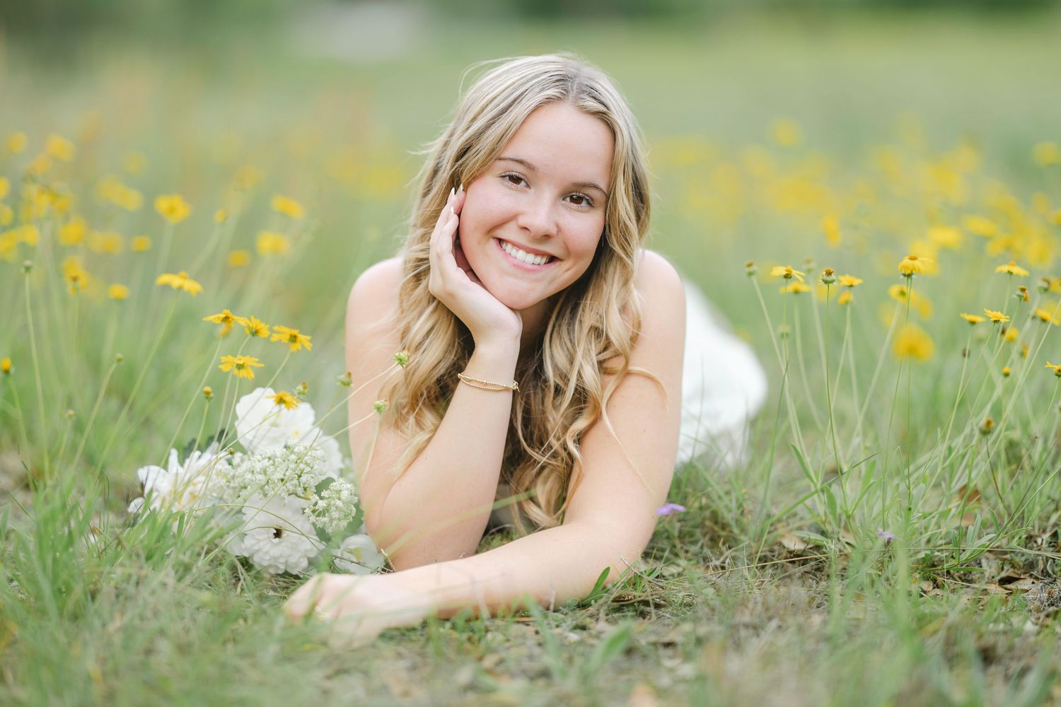 Young blonde woman lying in a sunny wildflower meadow with white blooms, smiling.