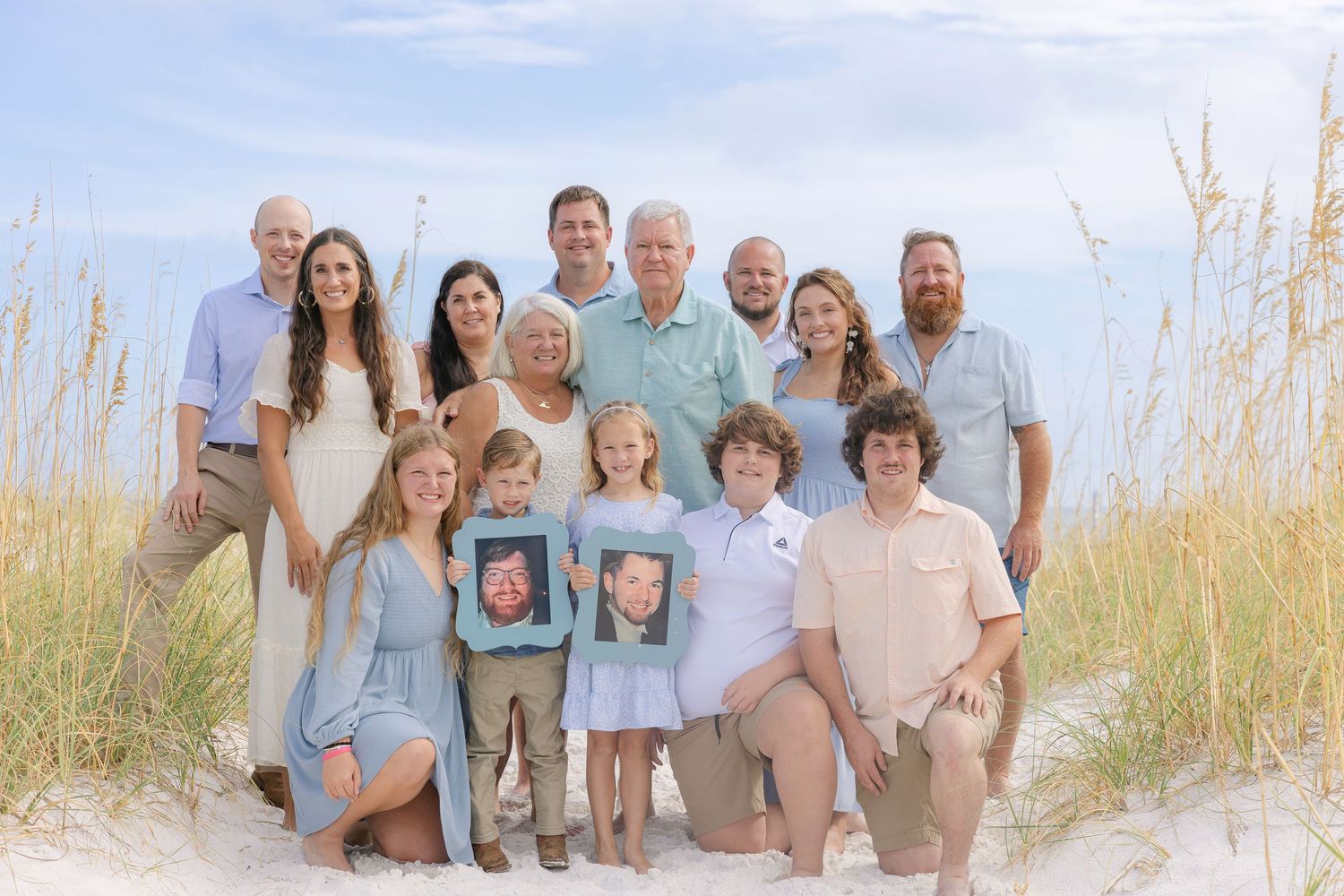 Multi-generational family group wearing coordinated light-colored outfits gathered on a beach at sunset.