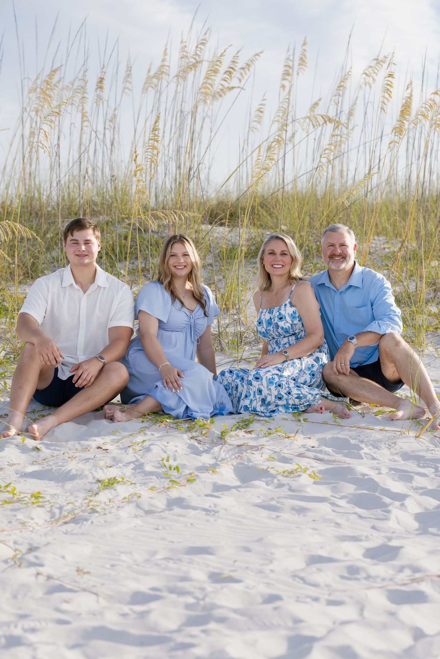 Happy family of four sitting together on white sand beach with sea oats.