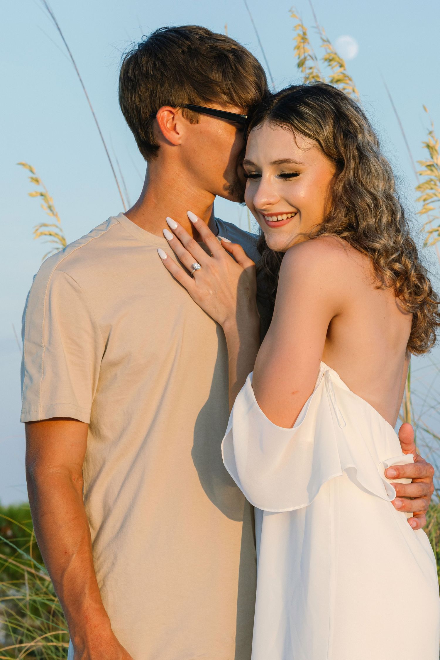 A romantic couple in white outfits embraces and laughs during an outdoor sunset photoshoot sequence.