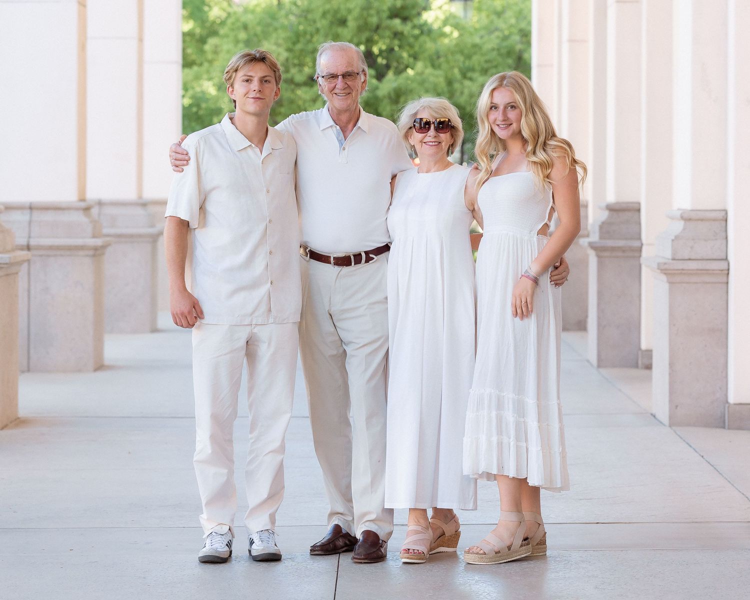 Family of four posing in white outfits between elegant columns outdoors.