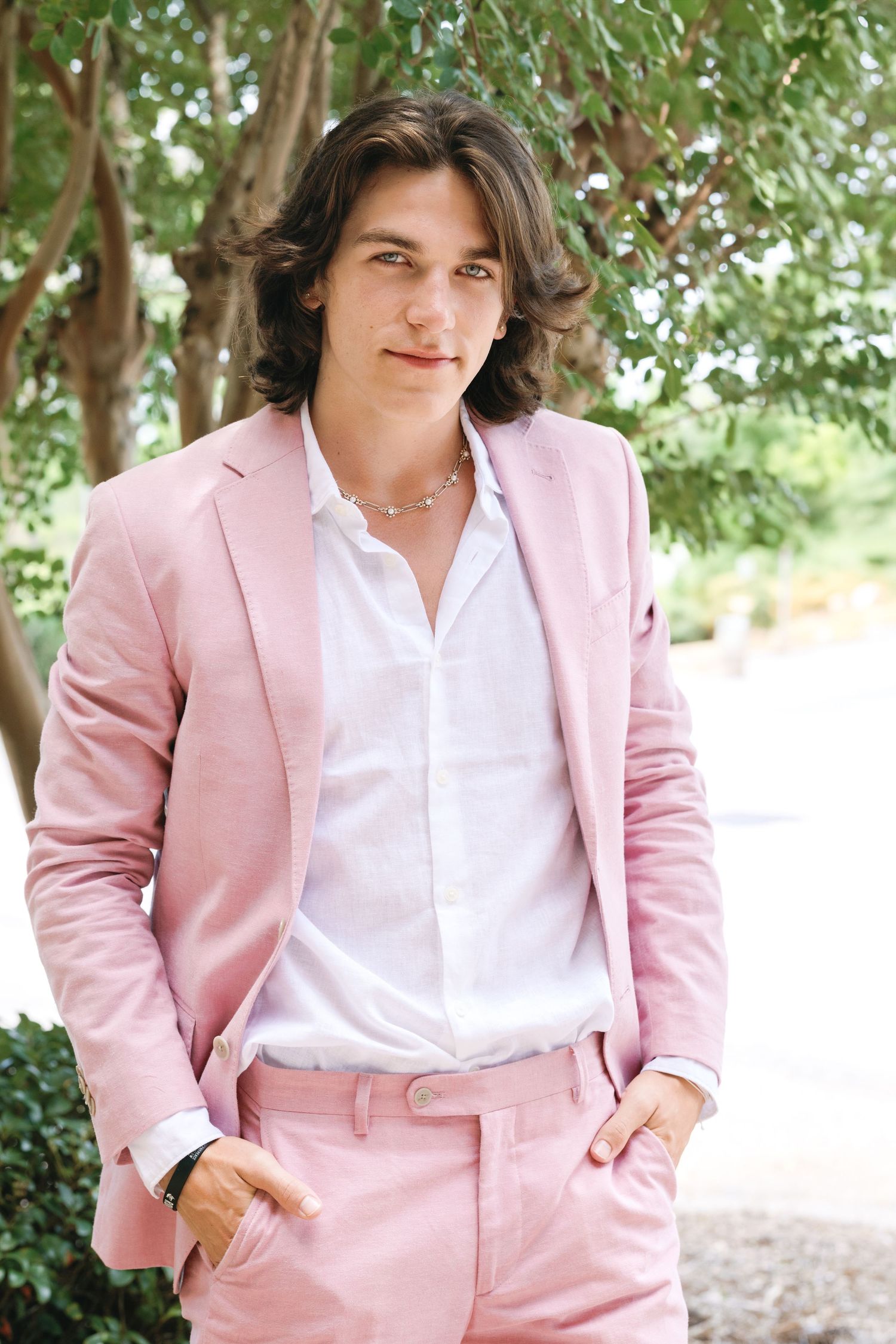 Person wearing stylish pink suit and white shirt poses outdoors.