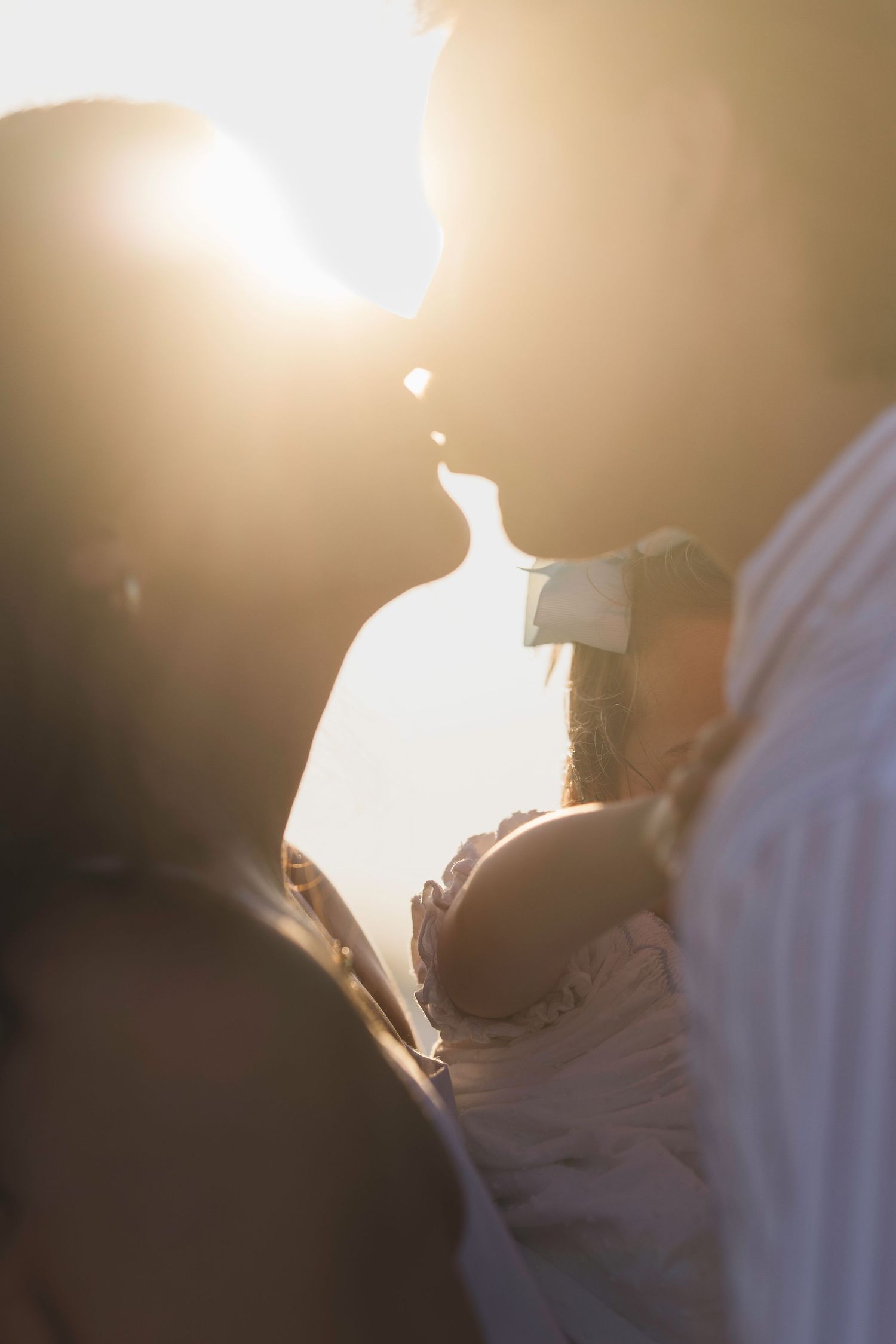 Couple sharing a romantic kiss backlit by golden sunset light.