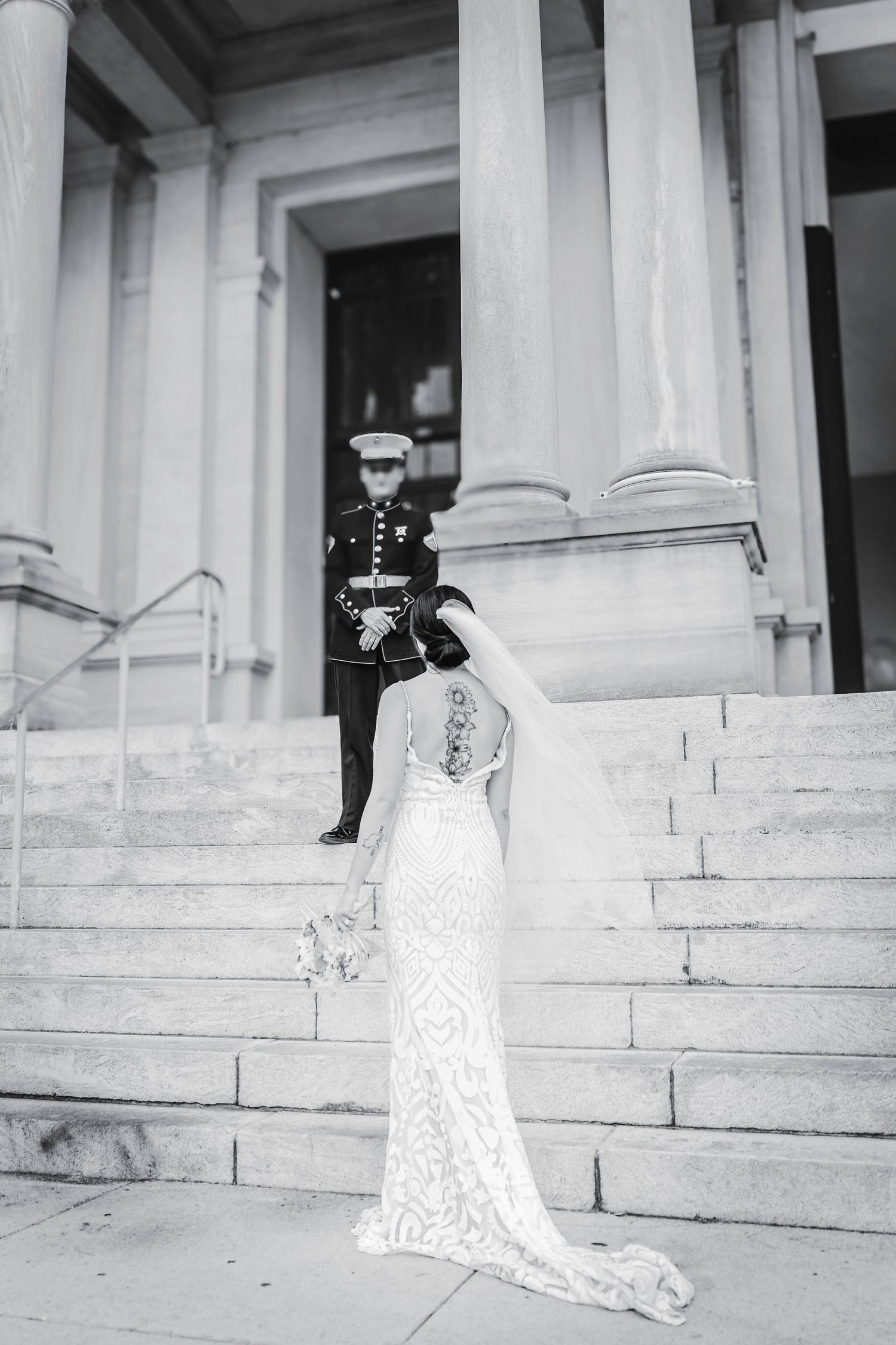 Bride in lace wedding gown walks toward Marine groom standing at top of grand stone steps.