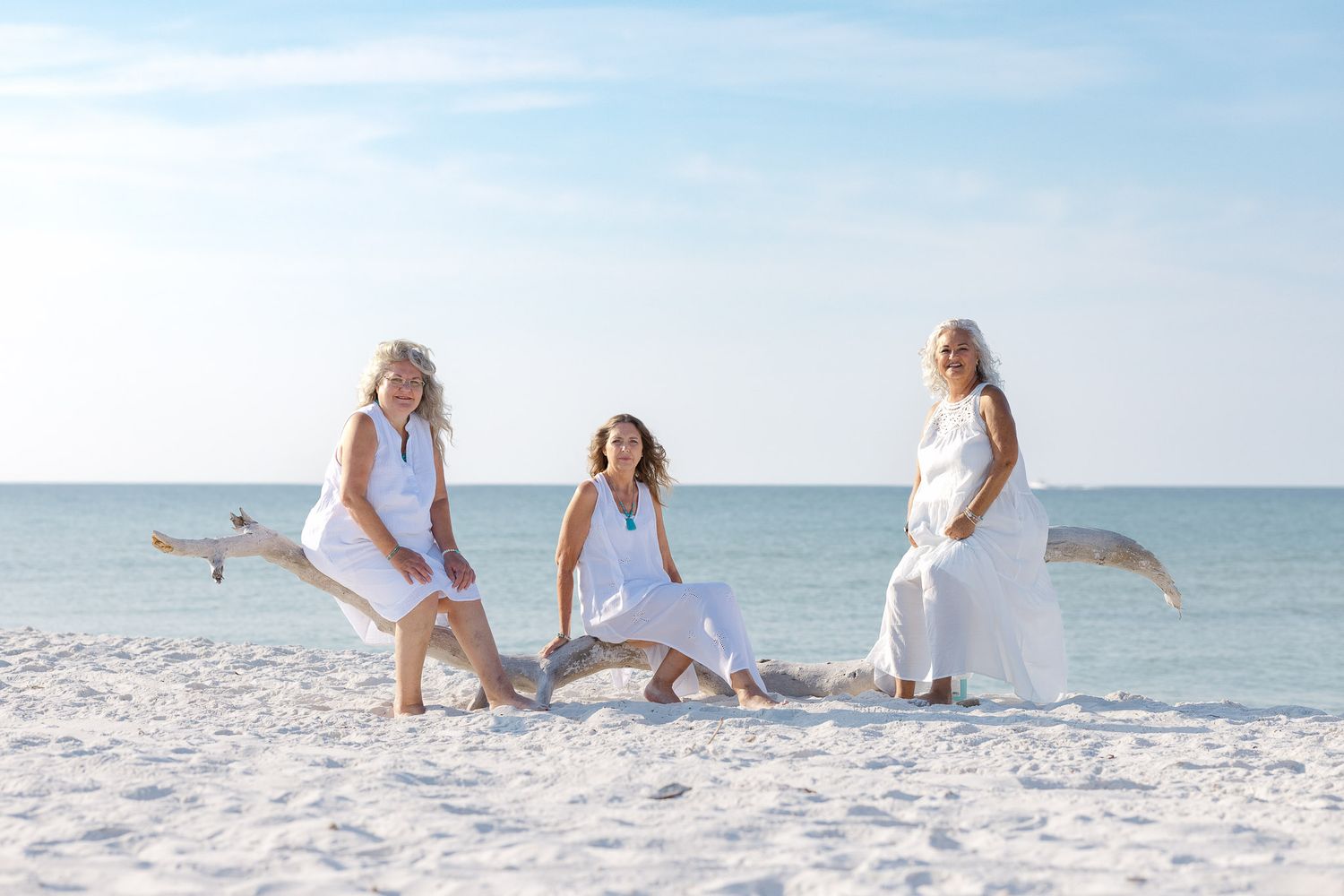 Group wearing all white outfits poses for fun candid photos together on a sunny white sand beach.