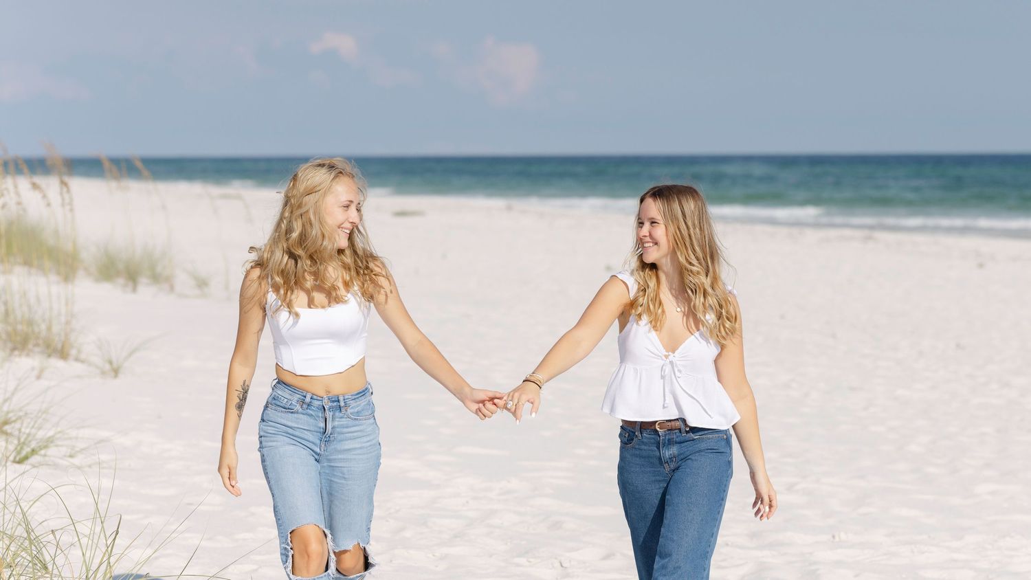 A group of women walk along a white sandy beach near the ocean while wearing casual summer attire.