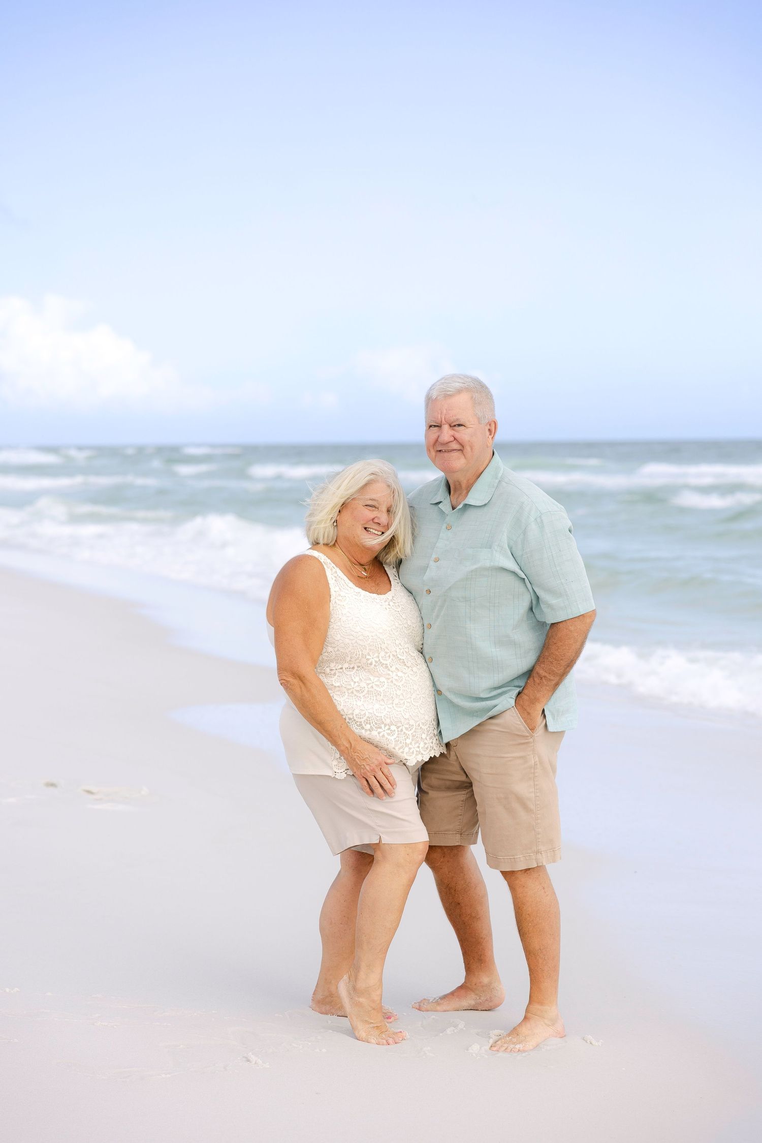 Couple sharing playful moments together on a sunny beach with ocean waves in the background.
