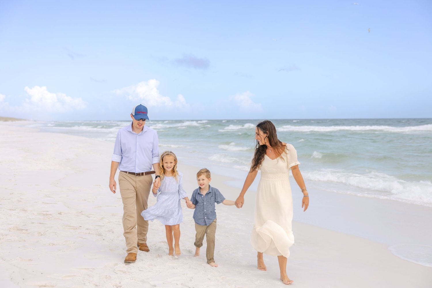 A family walks together along a sunny beach shoreline with ocean waves in the background.
