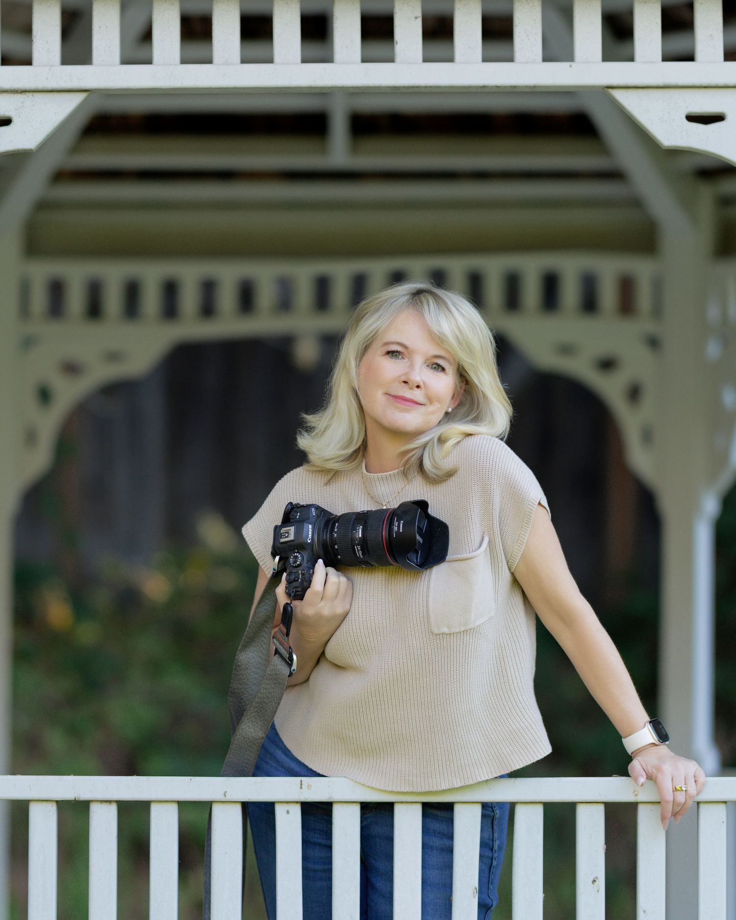 A photographer in a beige top leans against a white railing with camera equipment.