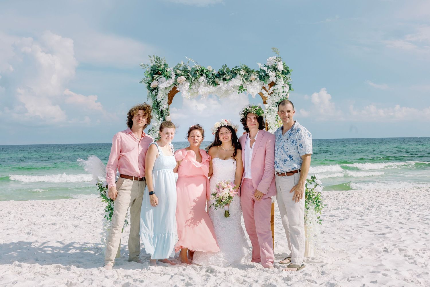 Group photo under beach wedding arch with pastel pink and mint green attire.