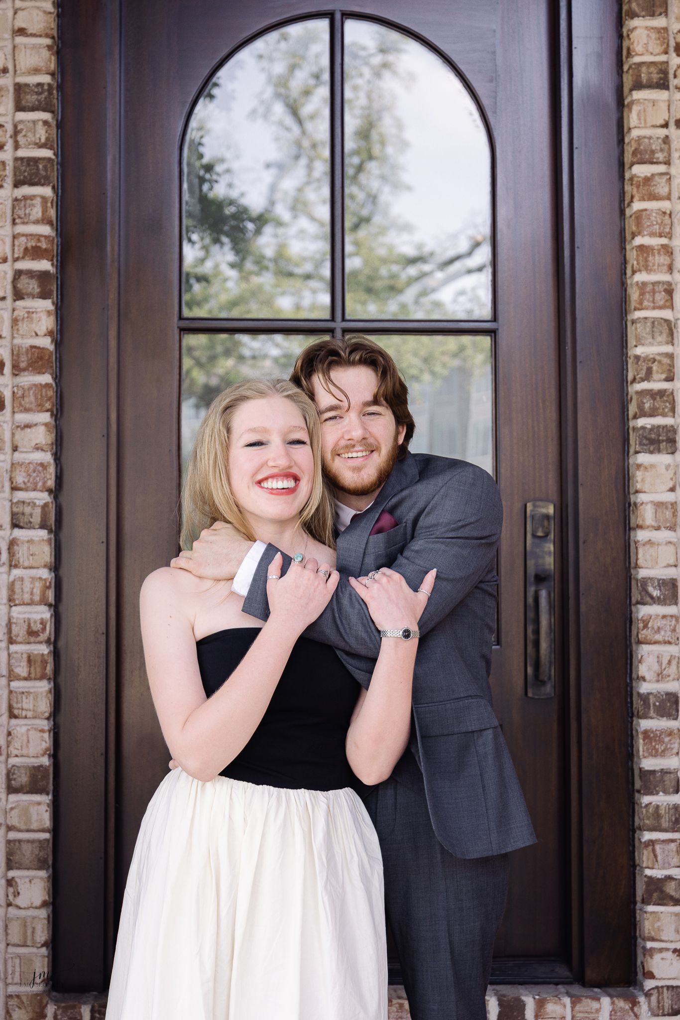 Couple poses together in formal attire in front of arched wooden door.