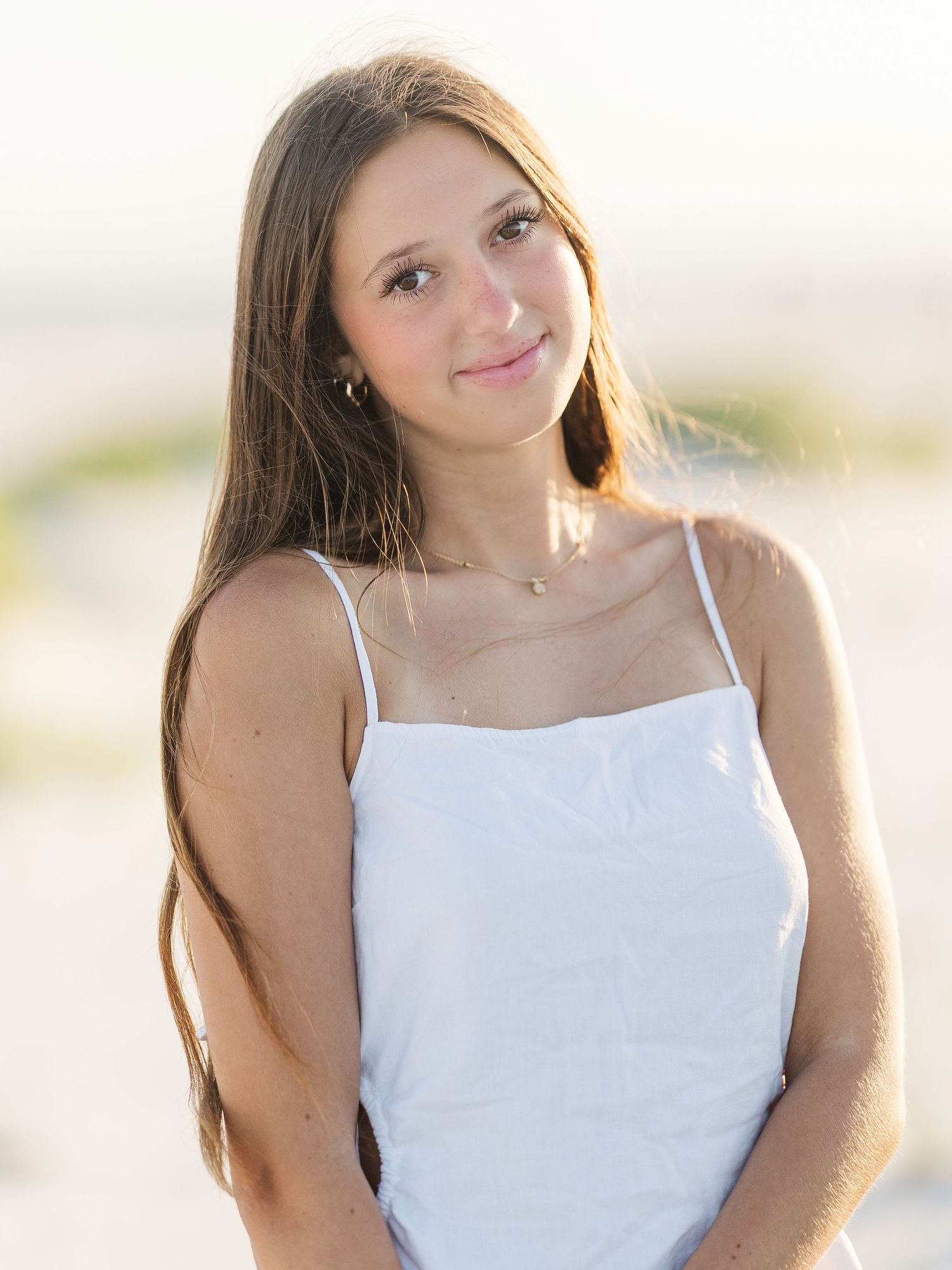 Portrait of a person wearing a white sundress on a beach during golden hour.