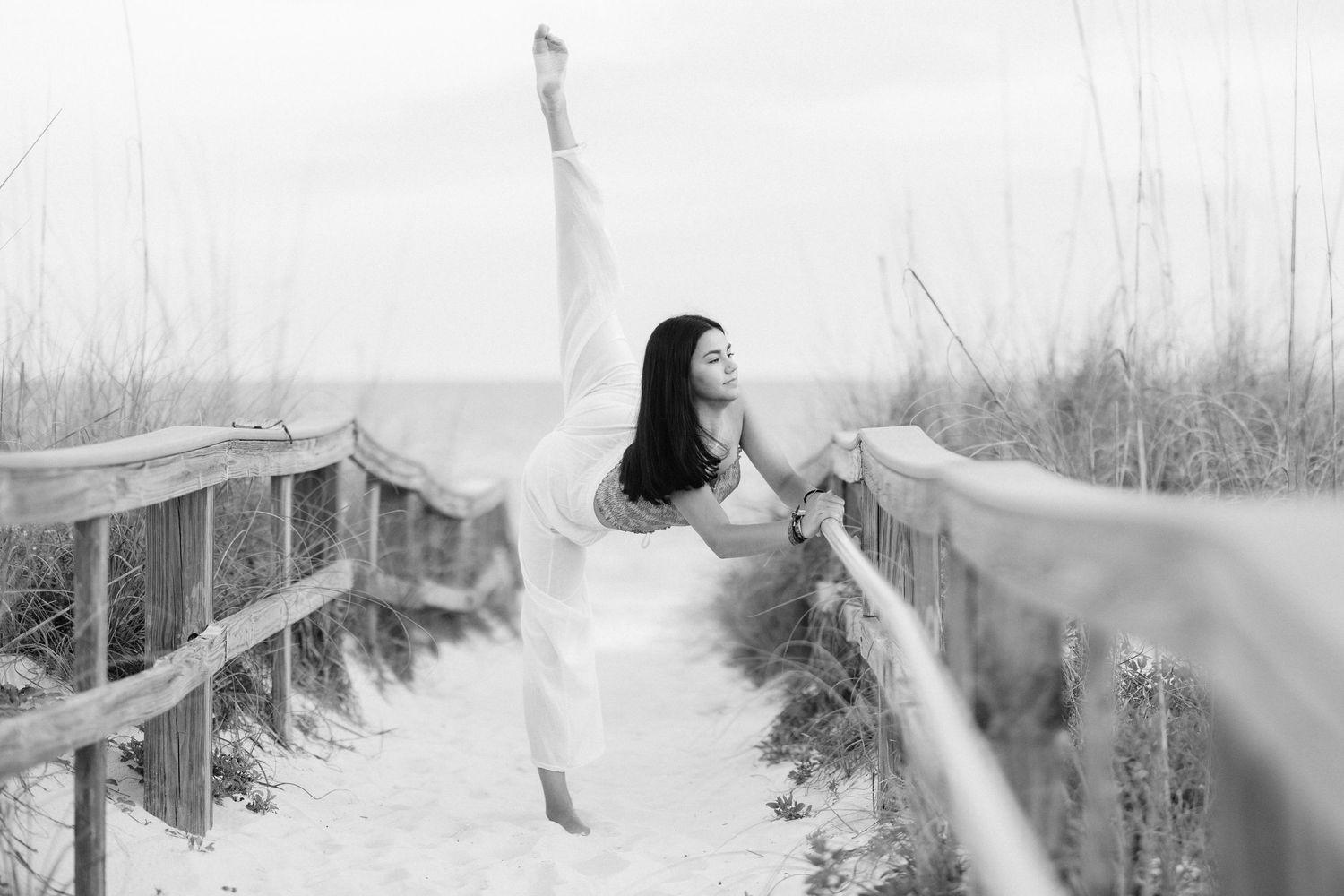 Black and white dance pose on wooden boardwalk overlooking beach dunes.