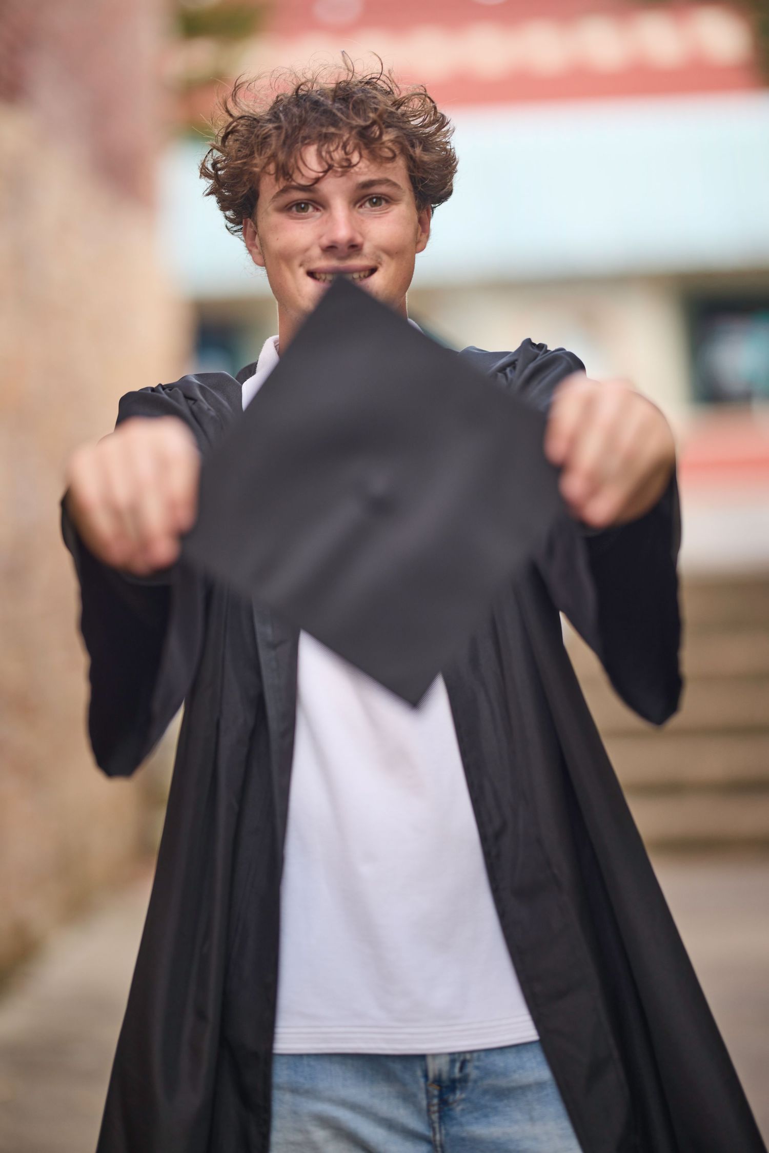 Graduate holding black graduation cap while wearing traditional black gown.