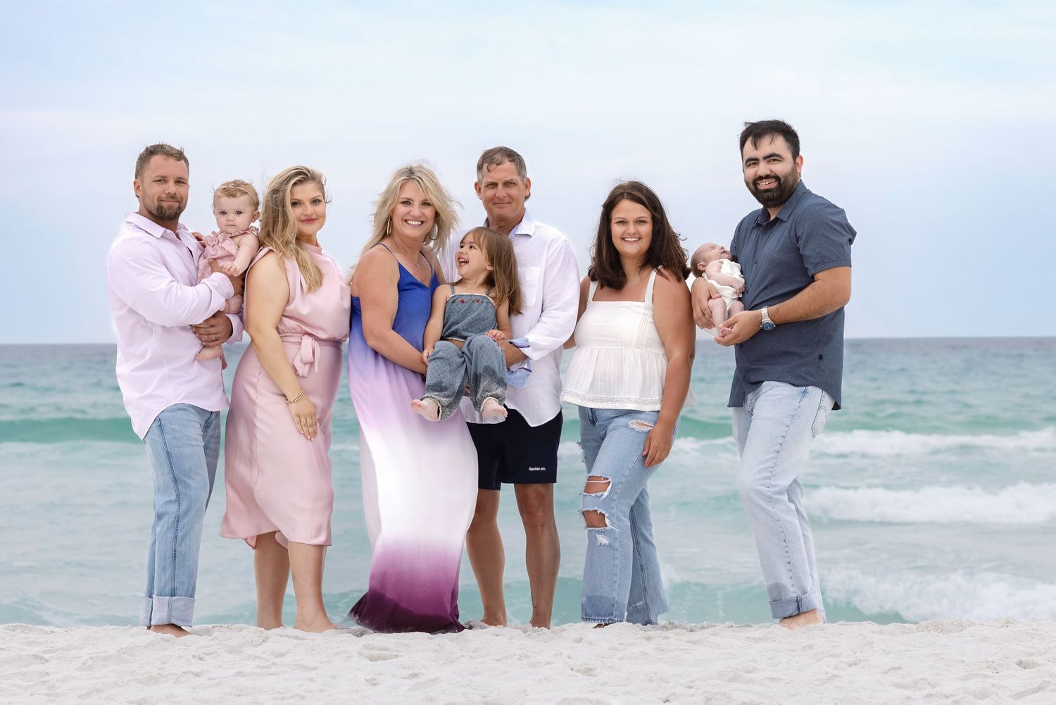 Large family group posing together on a sandy beach with turquoise ocean waves in the background.