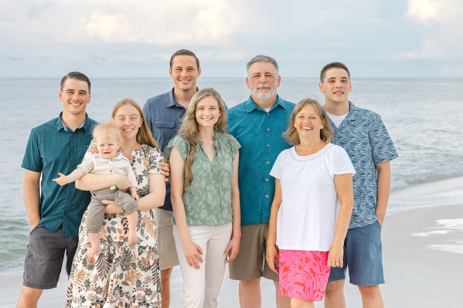 Group photo on sandy beach with ocean waves and cloudy sky in the background.
