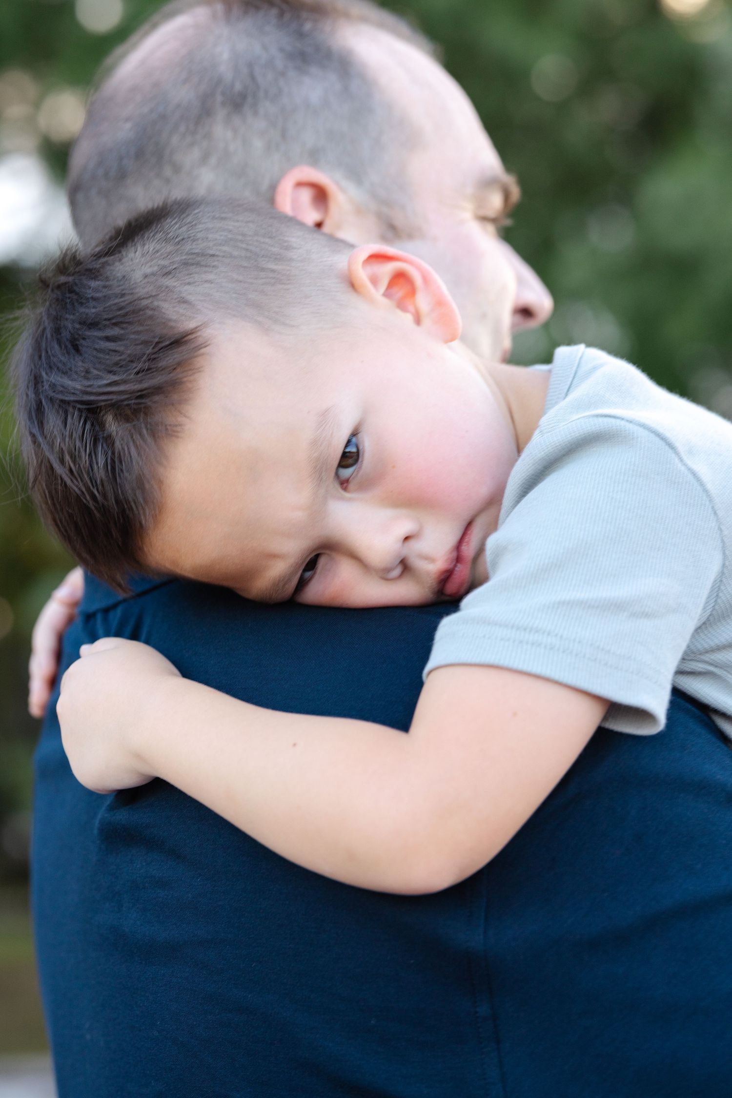Child rests head gently on shoulder in tender embrace against navy blue clothing.