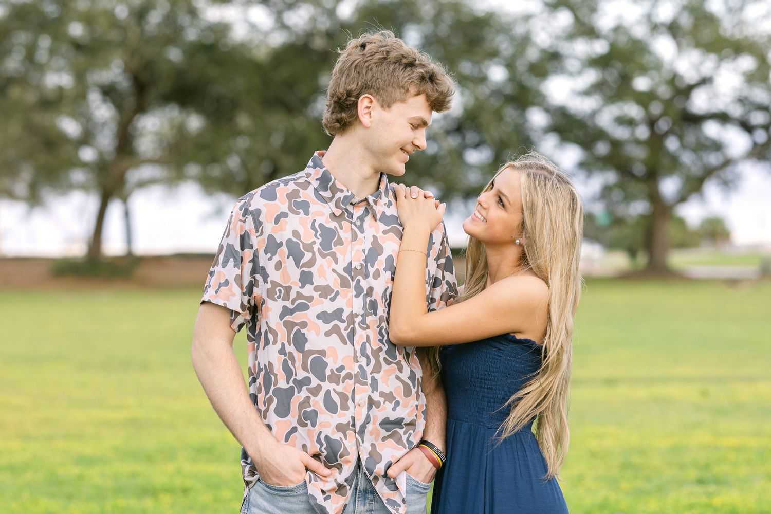 A couple shares tender moments together in a grassy field on a sunny afternoon.