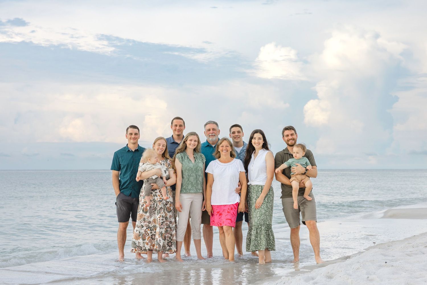 A cheerful family group poses together for portraits at sunset on a beautiful white sandy beach.