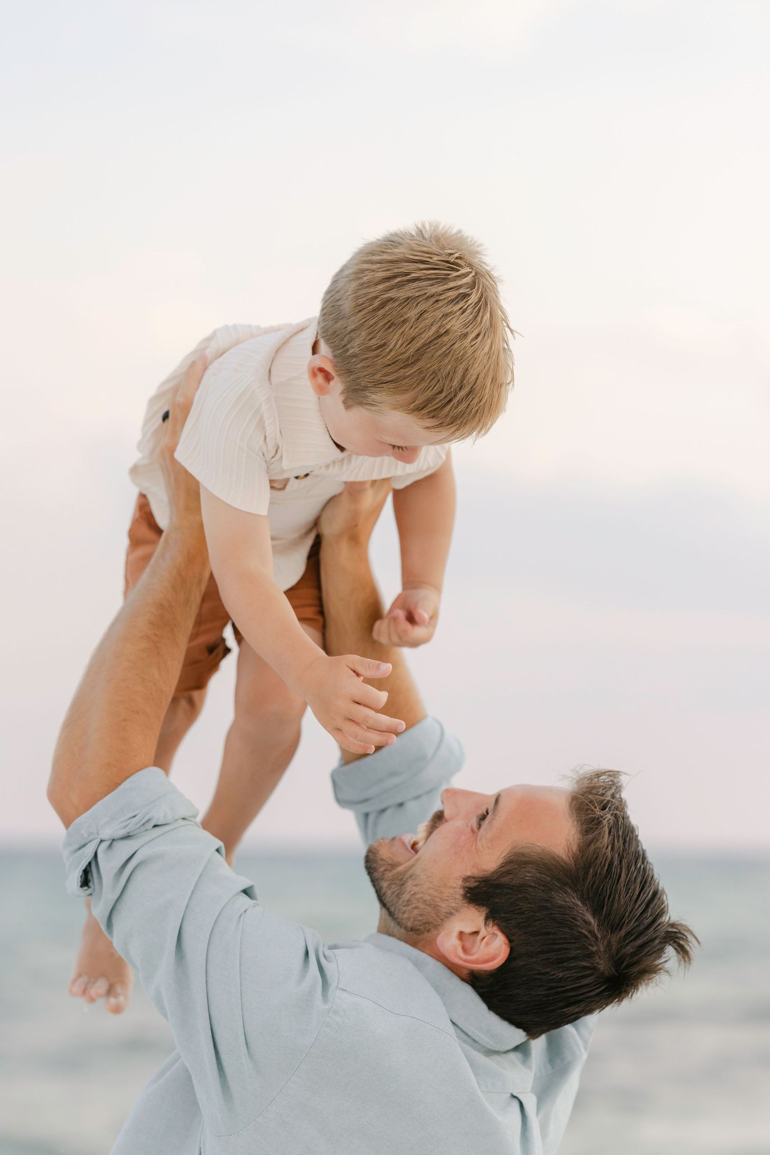 Parent and child share a playful moment lifting and bonding together against a bright sky background.