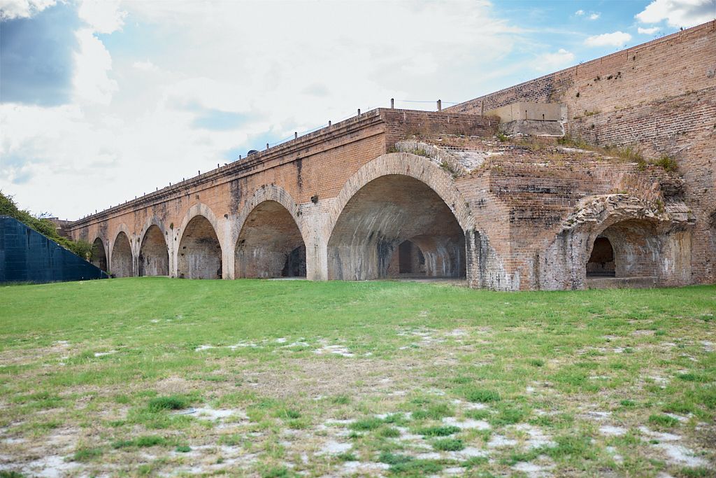 Ancient stone arches of a historic viaduct or bridge span across a grassy hillside under cloudy skies.
