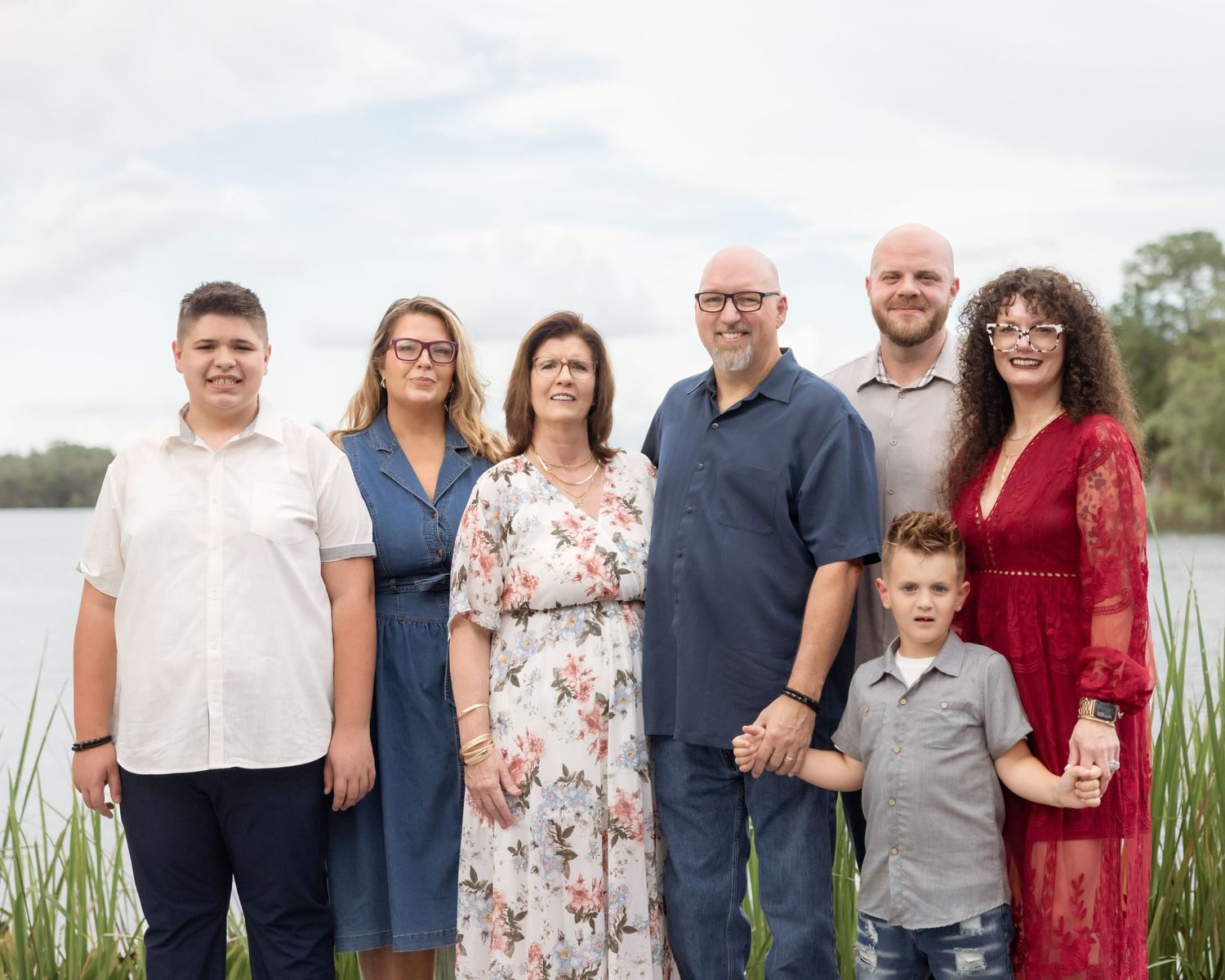 Family of seven posing outdoors near a lake, dressed in elegant attire for a professional family portrait.