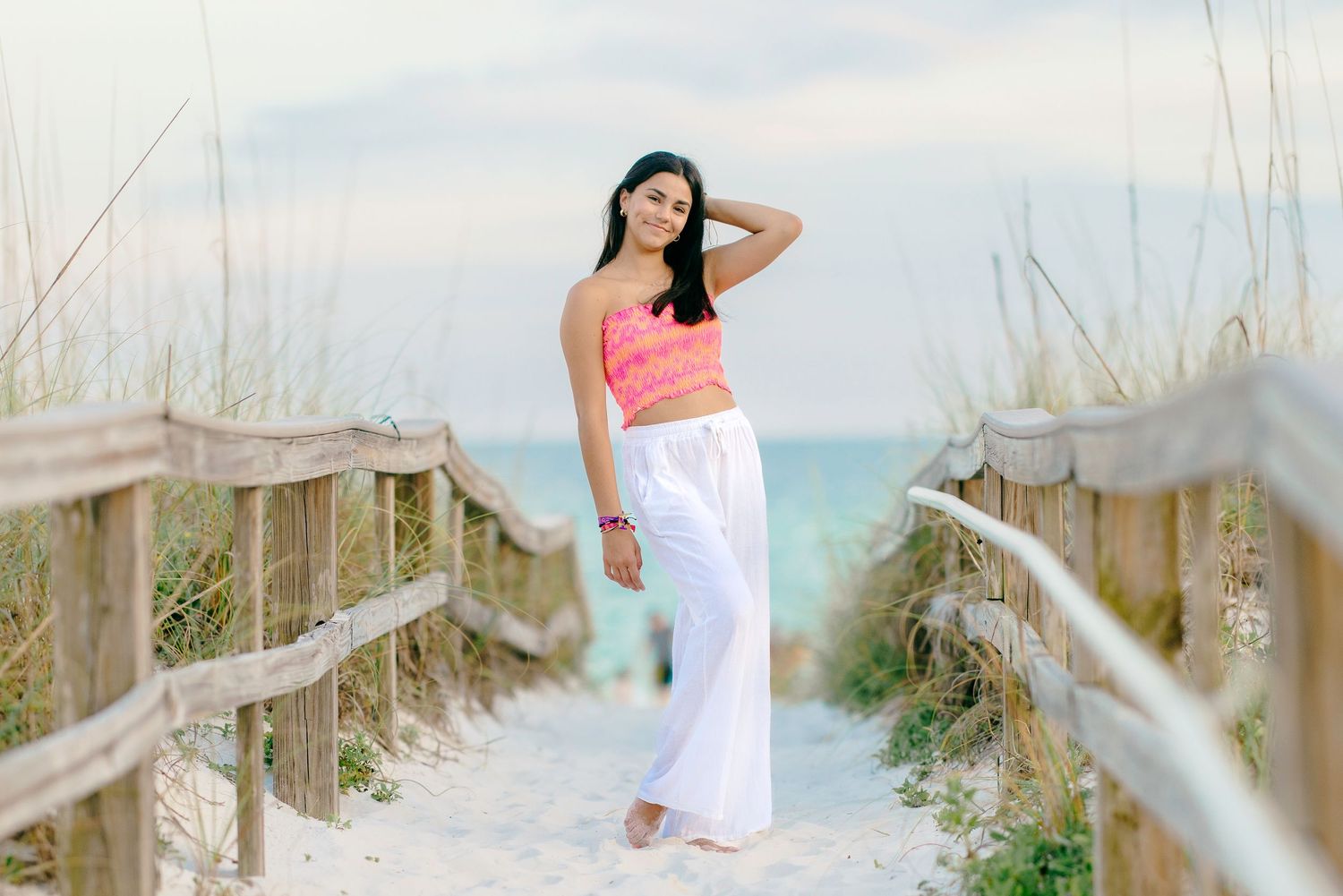 Casual pose on sandy beach boardwalk wearing summer attire with ocean view.