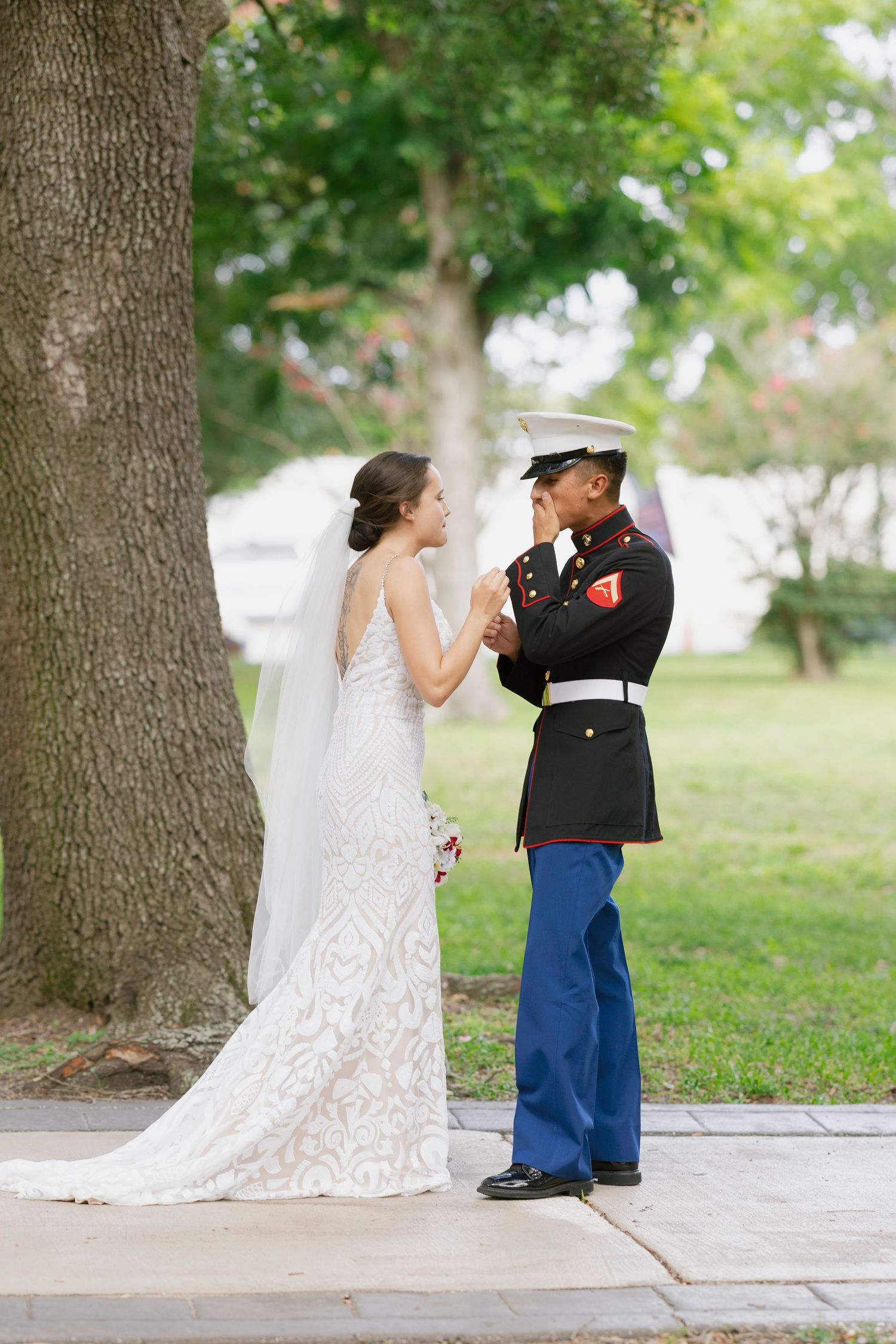 Marine groom emotional during first look with bride in lace wedding dress outdoors near tree.