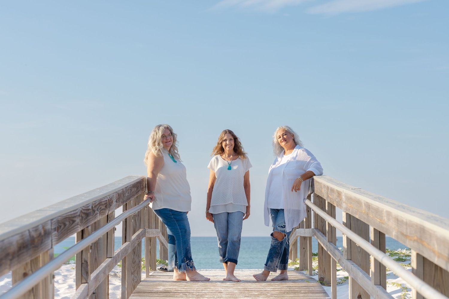 A family group walking together on a wooden boardwalk along a sunny beach coastline.