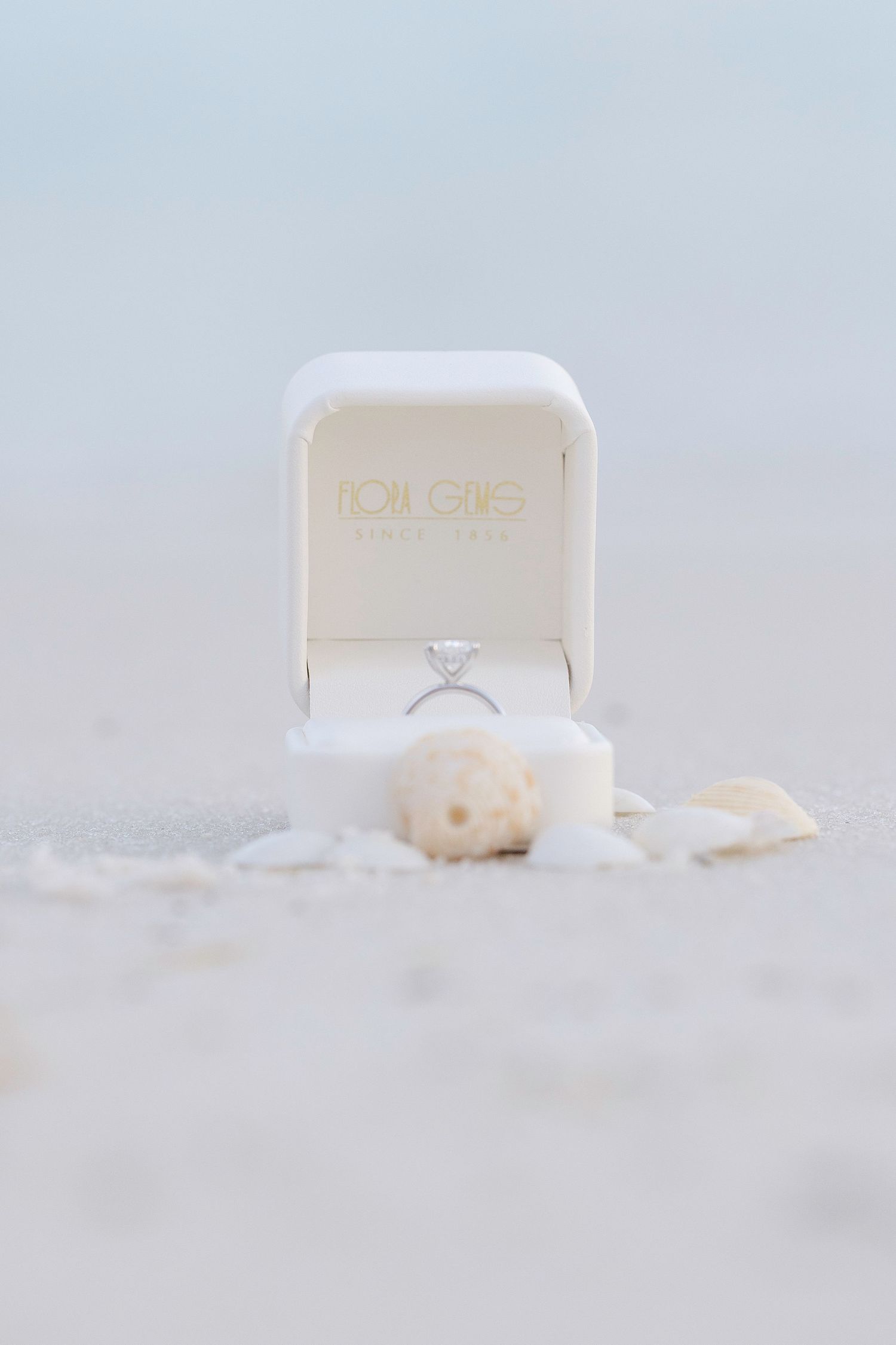 Elegant engagement ring box with soft feathers on light gray surface creates dreamy romantic atmosphere.