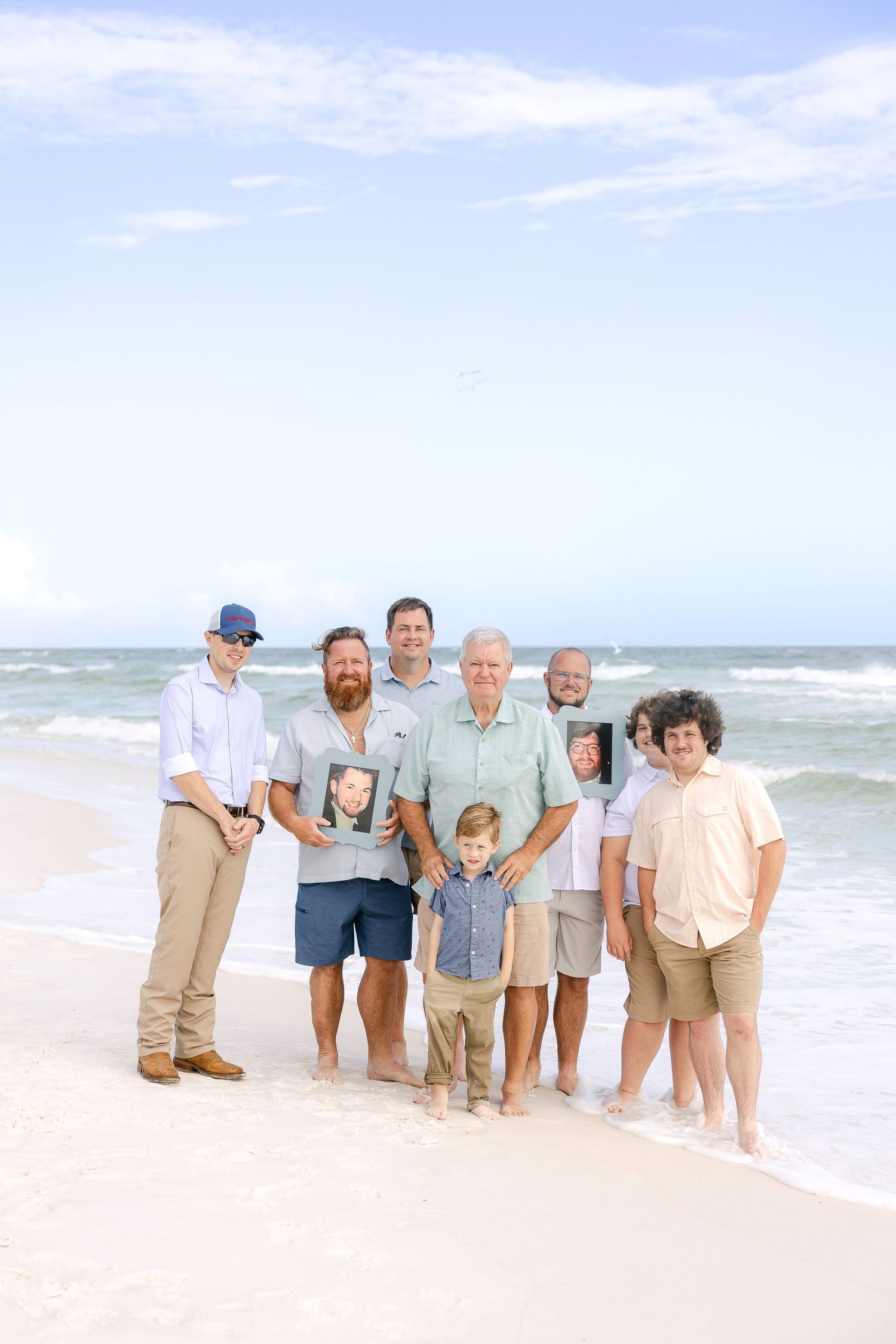 Extended family group poses casually together on beach wearing coordinated light colored clothing.
