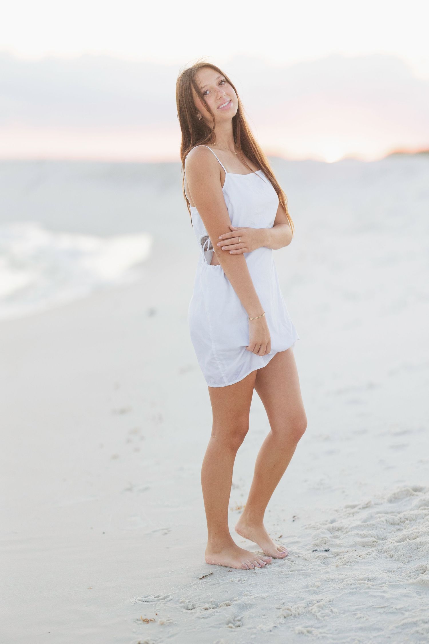 Woman in white swimsuit poses gracefully on sandy beach during sunset creating artistic silhouette effect.