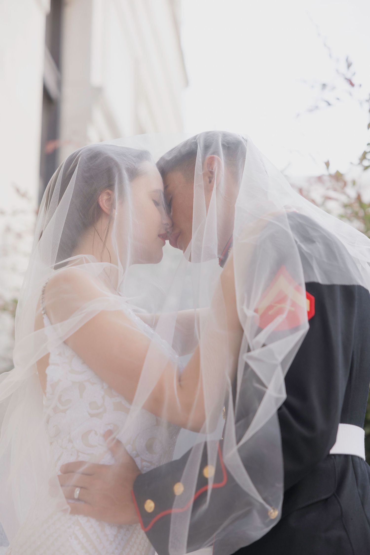 Bride and groom sharing an intimate moment under a flowing white veil on their wedding day.