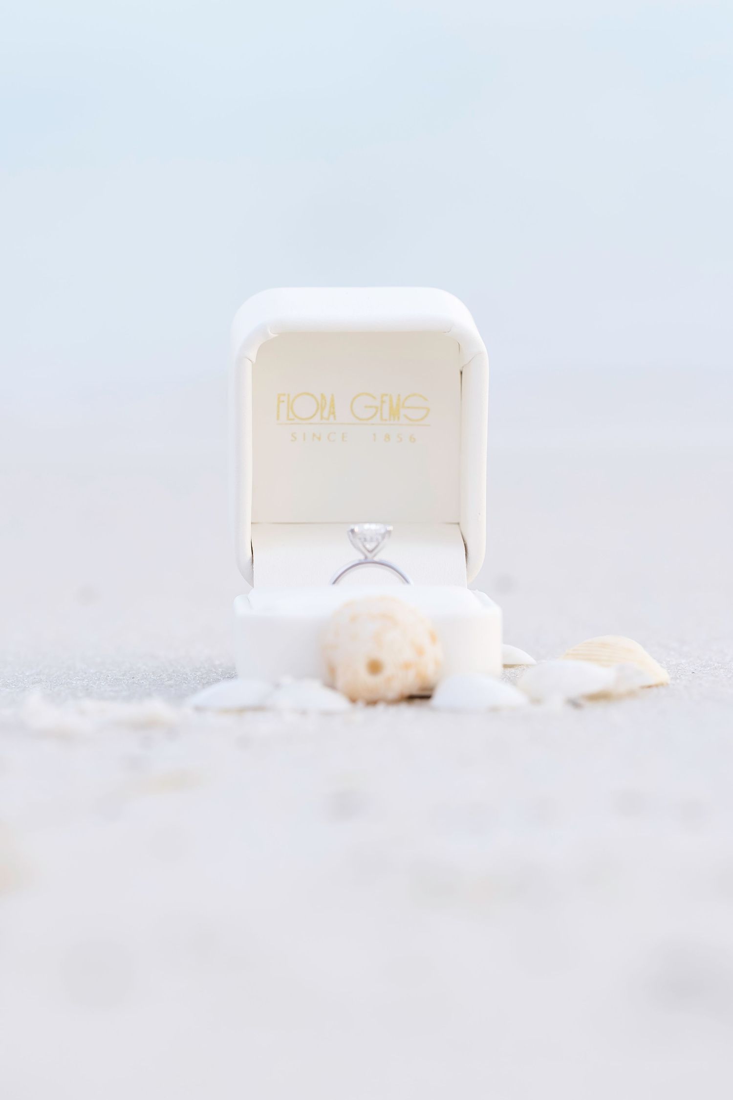 Diamond engagement ring nestled in white snow with ring box in soft light setting creating romantic winter atmosphere.