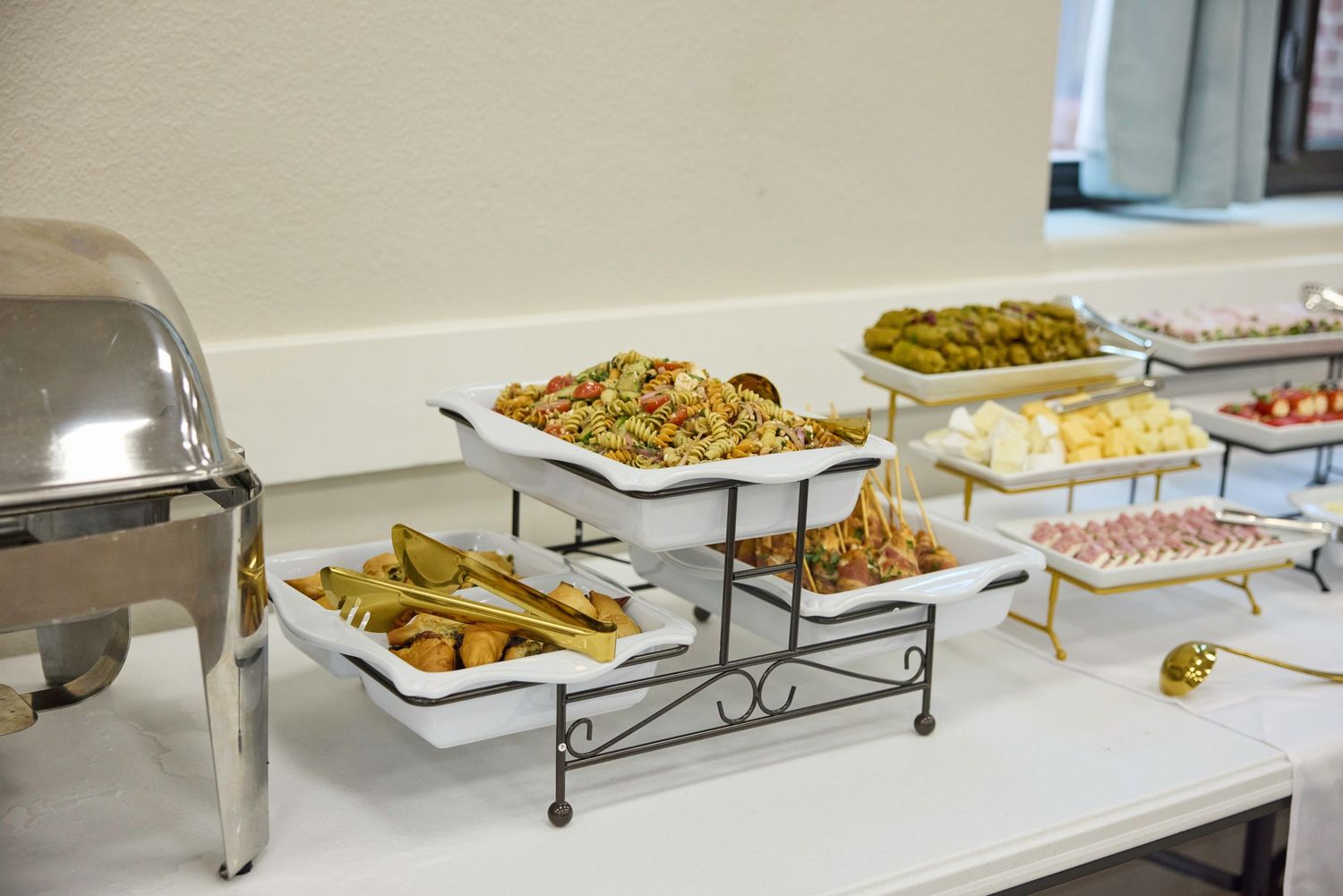 Catering buffet setup with metal serving trays displaying various hot dishes and appetizers on tiered stands.