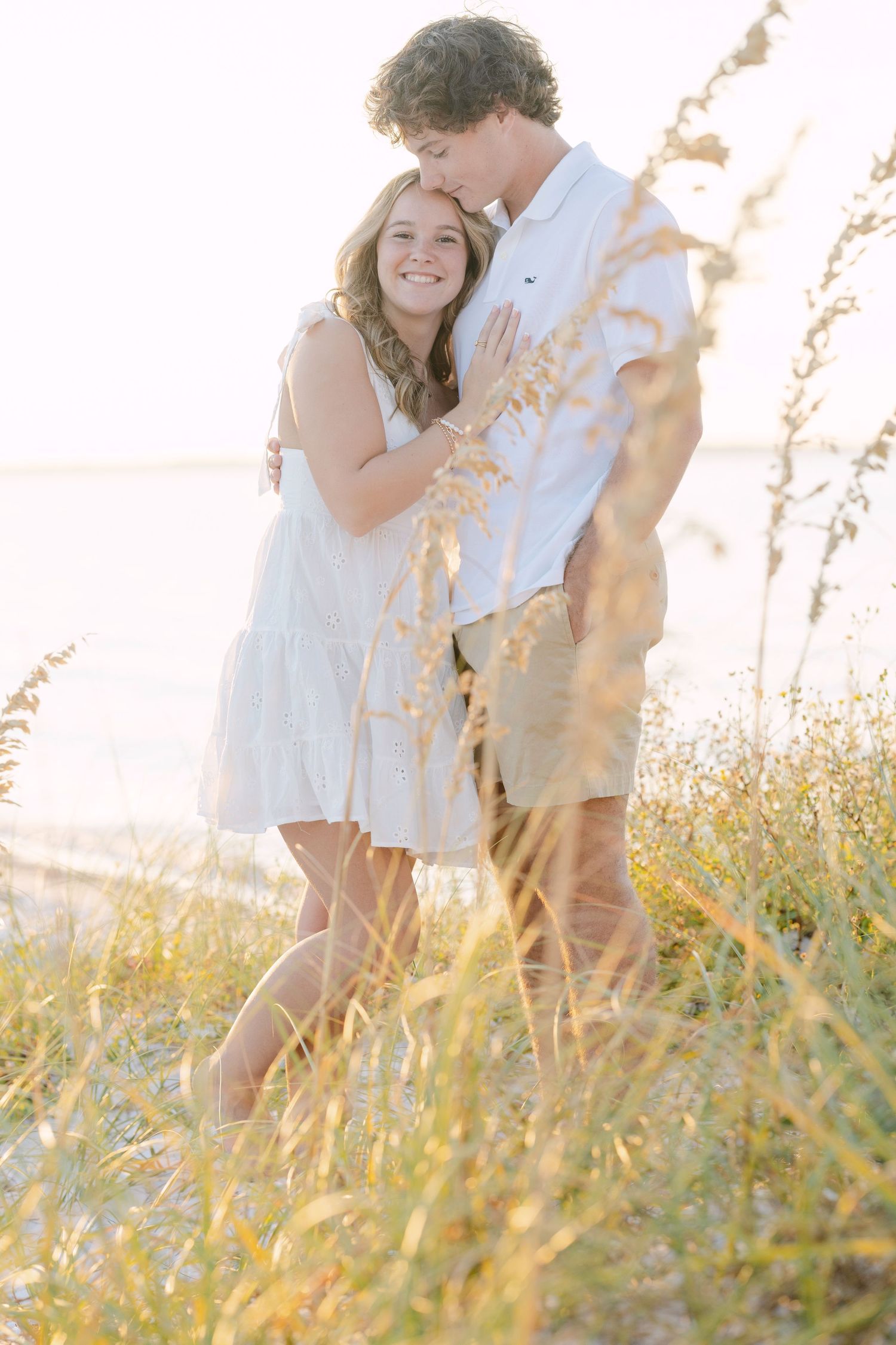 A couple embraces in a sun-lit meadow of tall grass and wildflowers during golden hour.