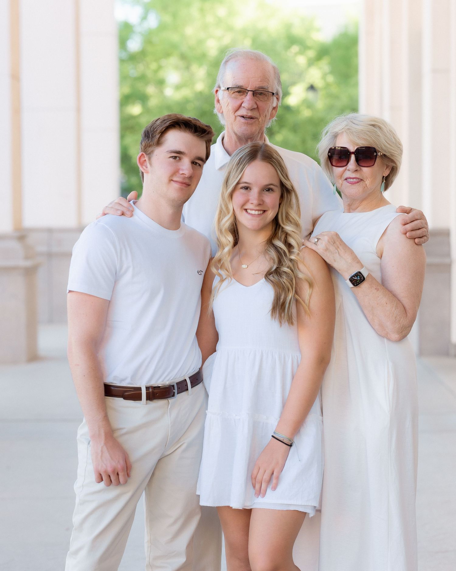 Family of four posing in white outfits for a portrait photo outdoors.