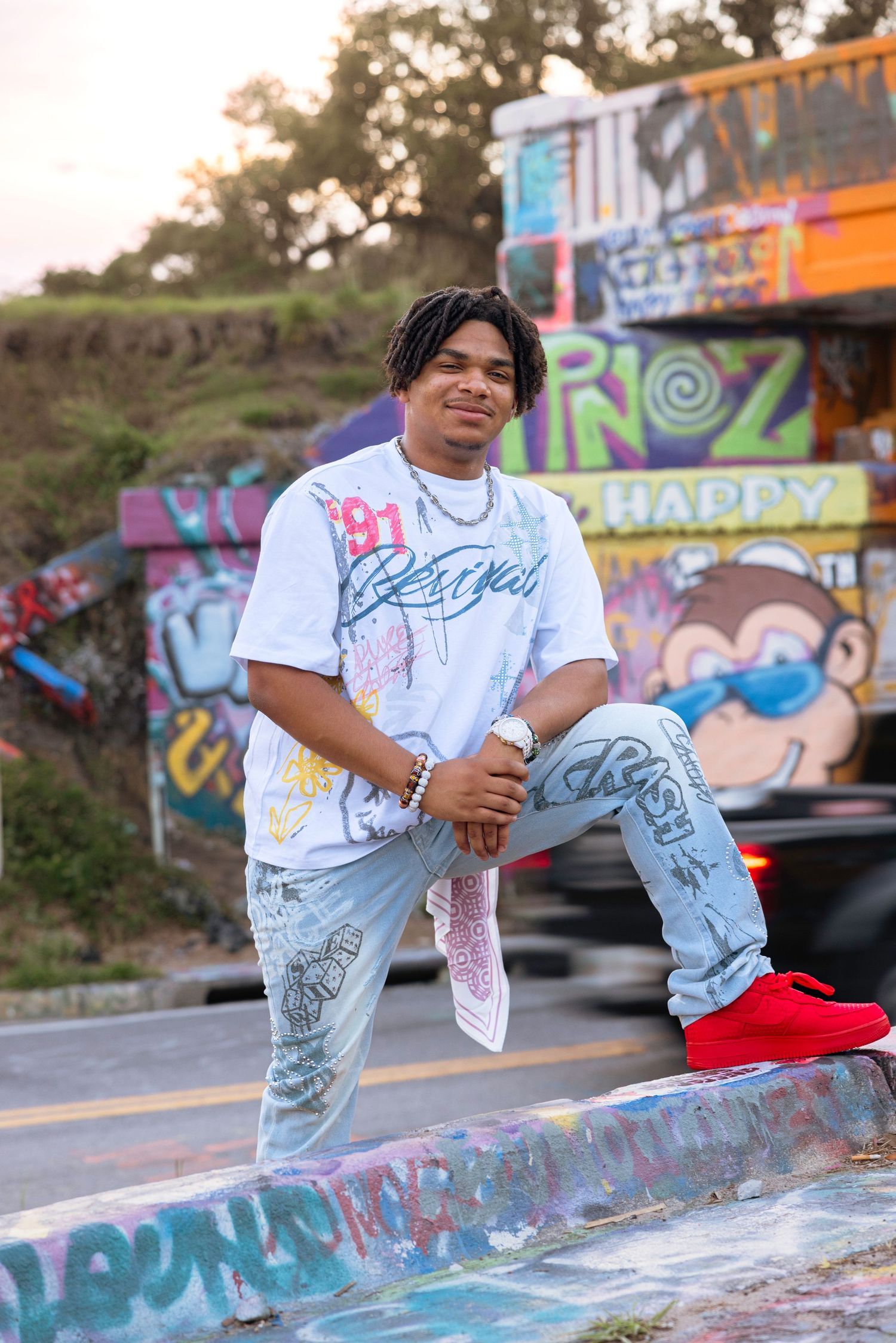 Young man in graphic tee, light jeans, and red sneakers posing confidently in front of colorful graffiti wall.
