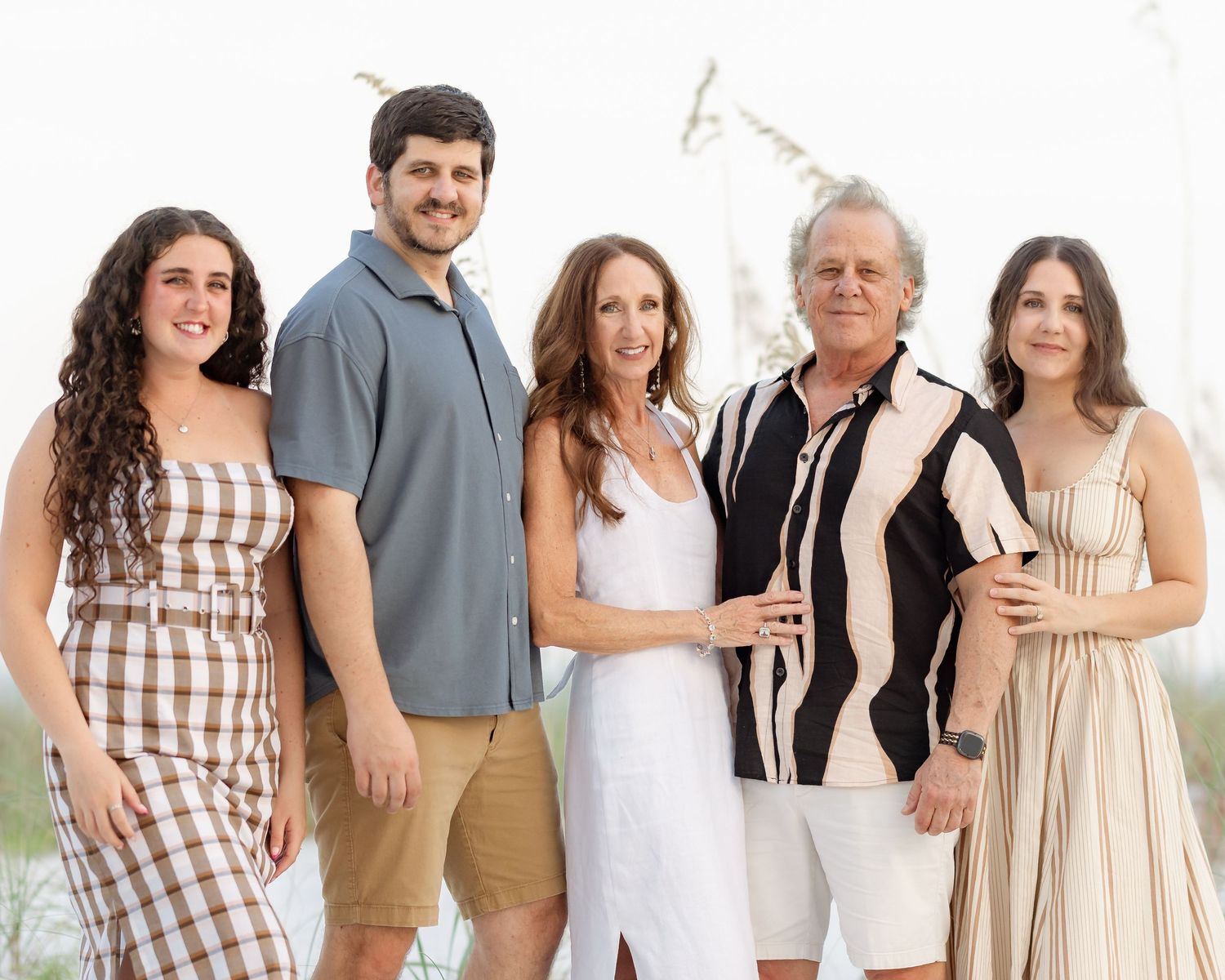 A happy family of five poses together outdoors in coordinated outfits for a bright and elegant beach photo session.