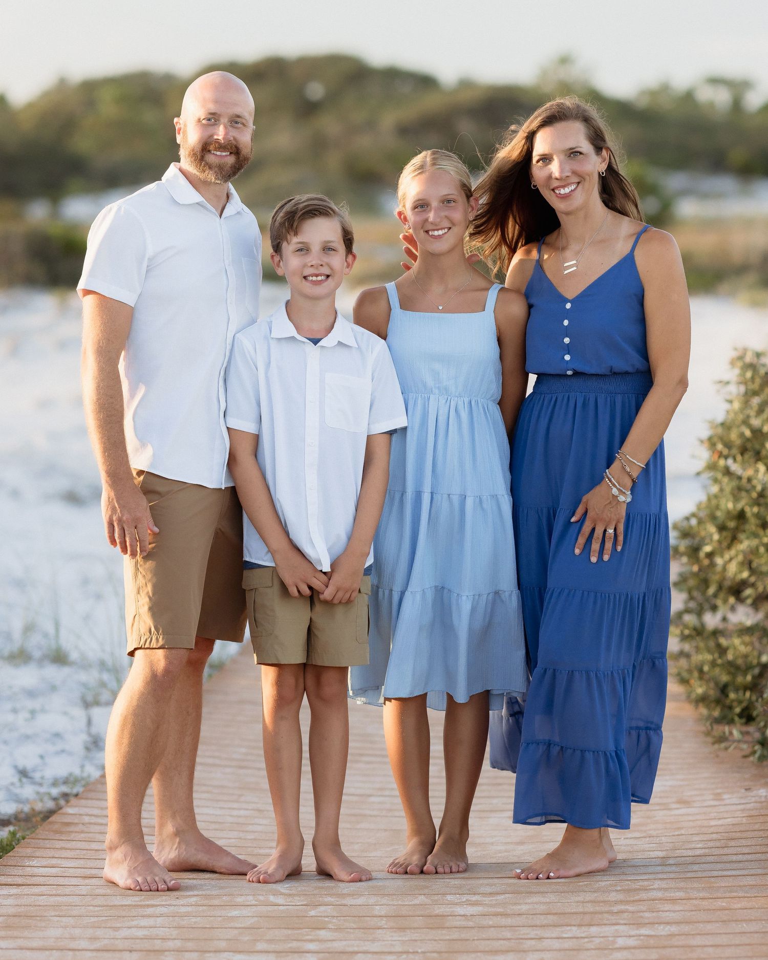 Happy family of four posing together on a beachside boardwalk at sunset.