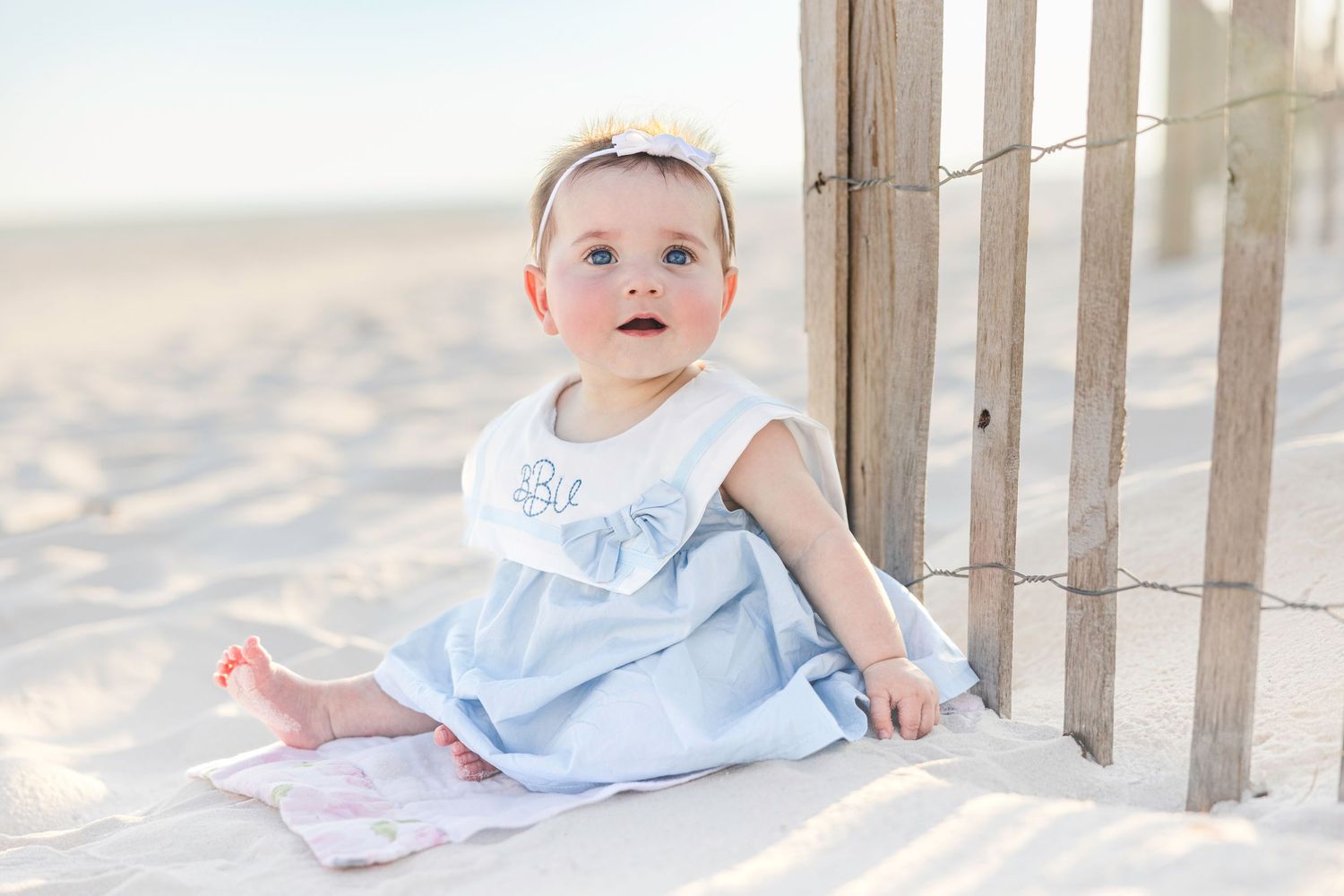 Baby in white christening gown crawls and plays on sandy beach at sunset in series of connected images.