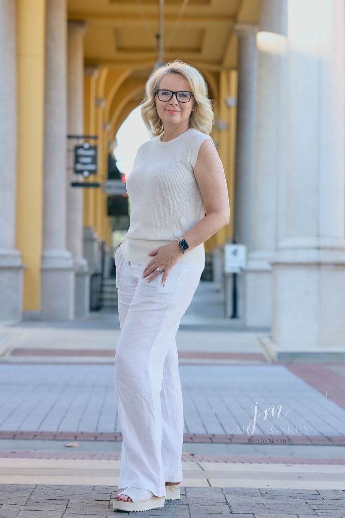 A person wearing an all-white casual outfit with glasses stands in front of a building with columns.