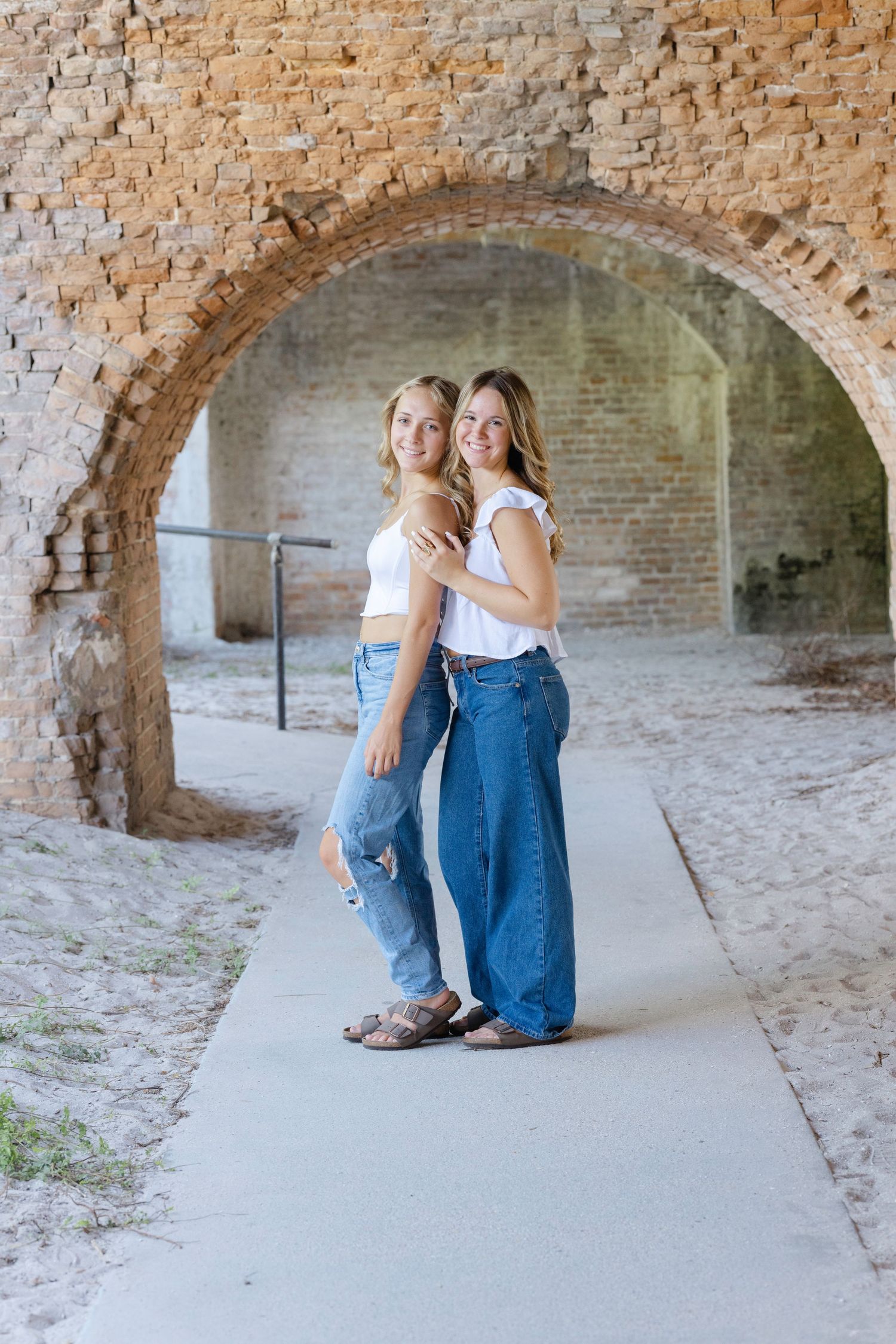Two people sit casually in a historic brick archway at Fort Pulaski, with a series of vaulted corridors visible behind them.