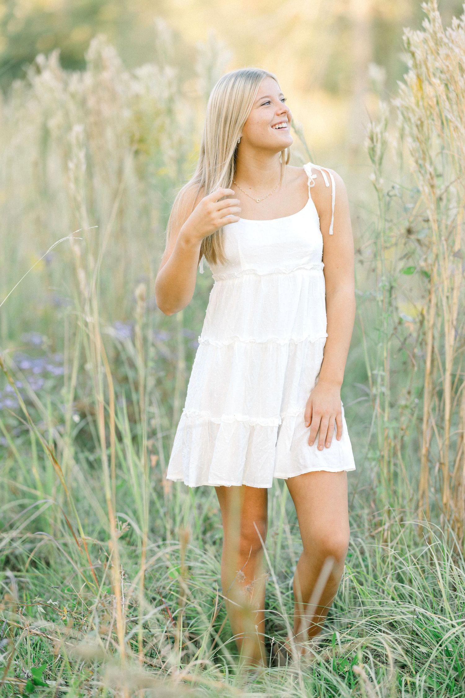 A person in a white summer dress stands among tall wildflowers in a sun-drenched meadow at golden hour.