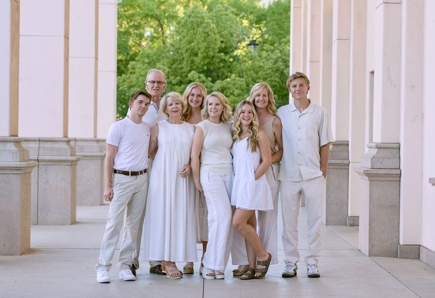 A group of people dressed in coordinating white outfits pose together in front of a beige outdoor colonnade.