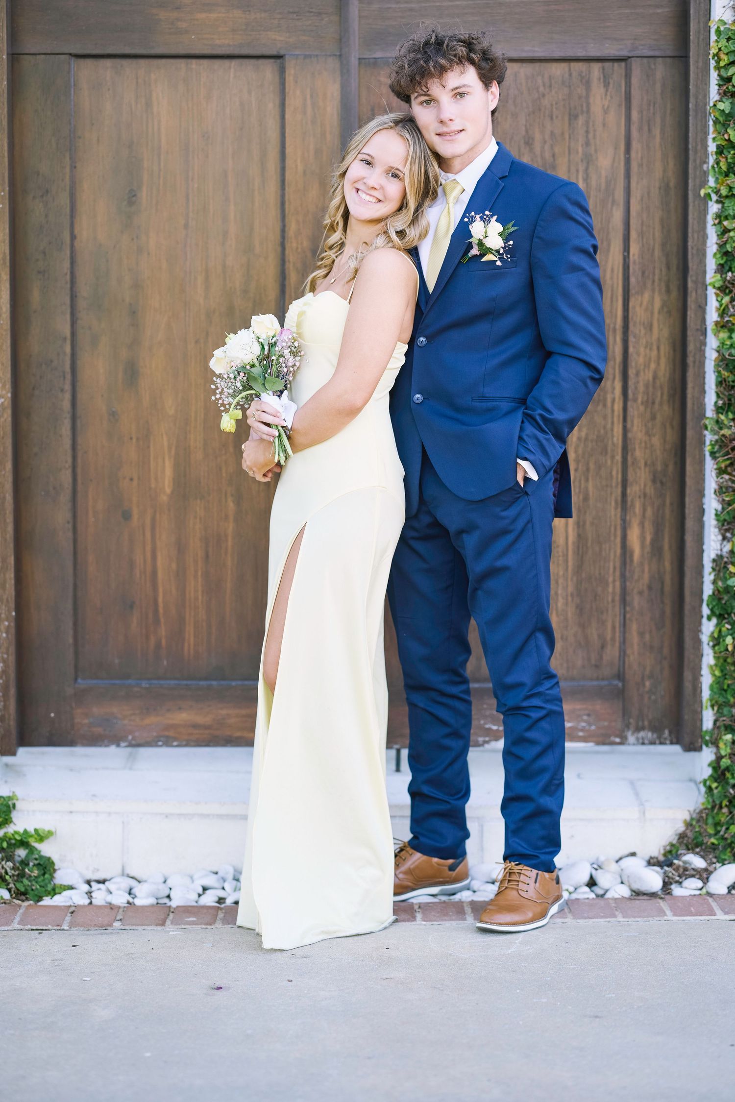 A couple poses together against a rustic wooden door backdrop in wedding attire.