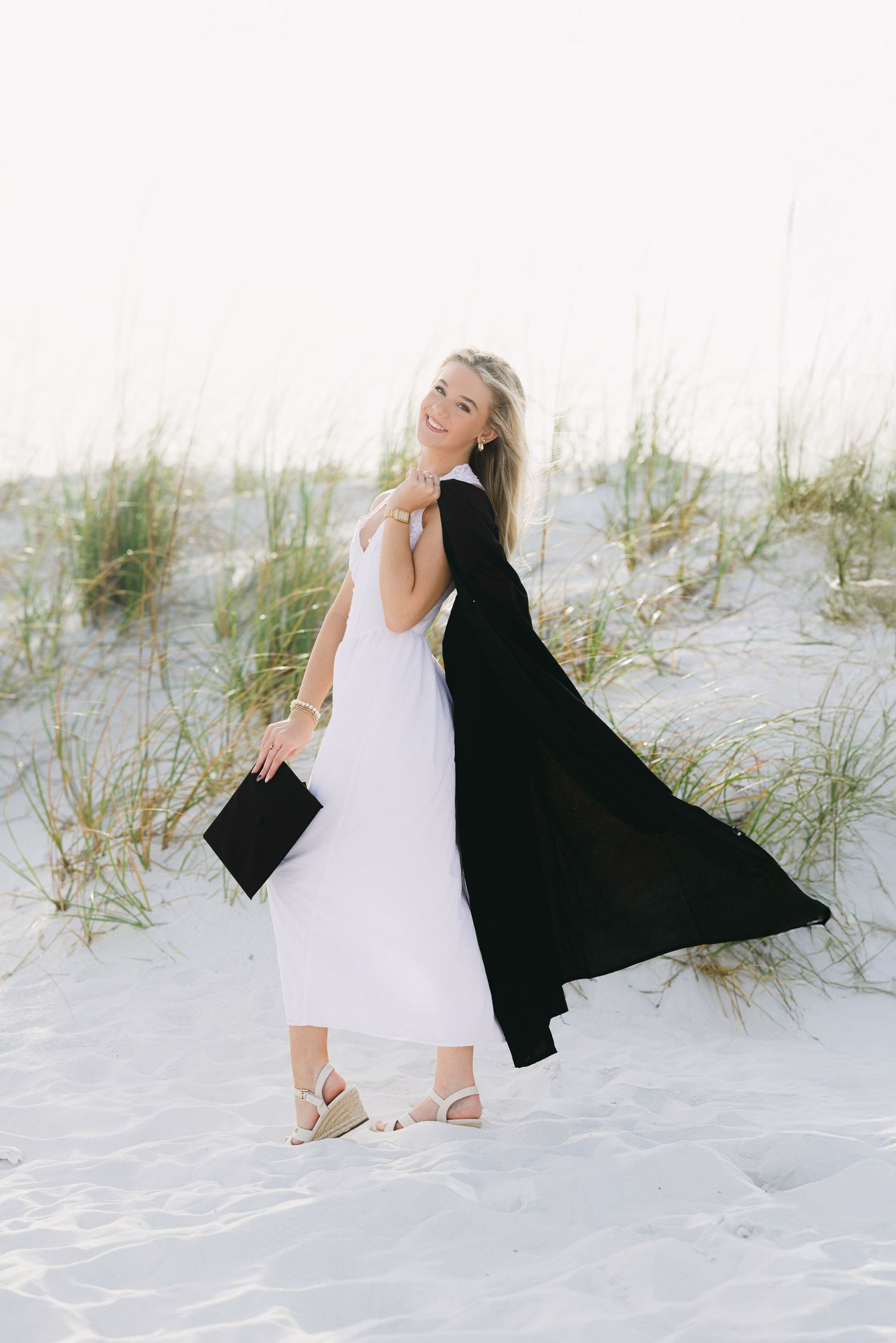 A person in a white dress poses gracefully on white sand dunes with a flowing black shawl creating artistic movement.